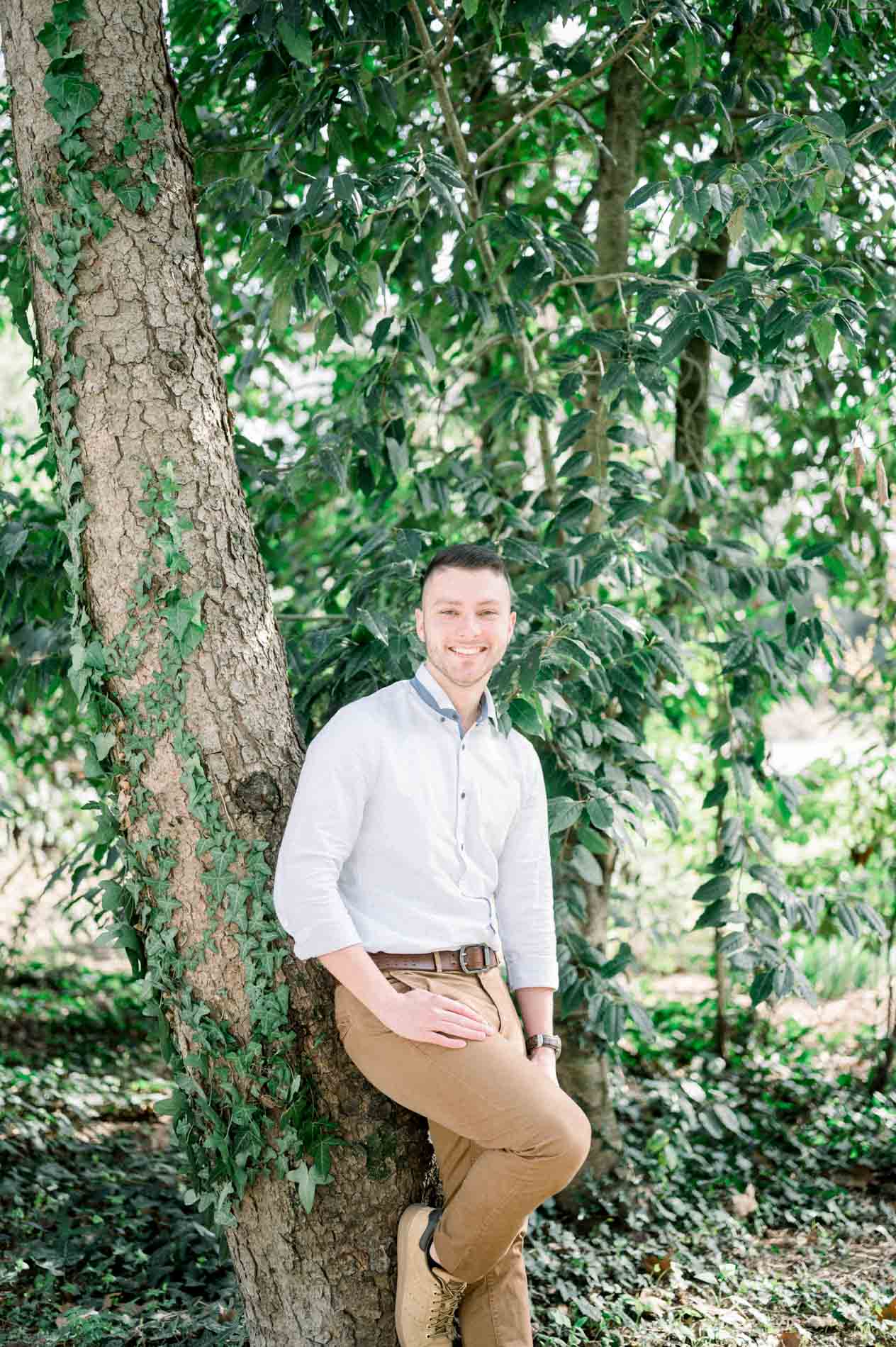 The brother in a white shirt leaning against an ivy-covered tree