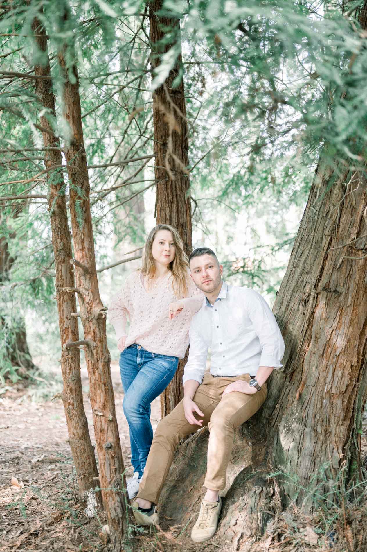 Brother and sister leaning against a large tree in the park's woodland