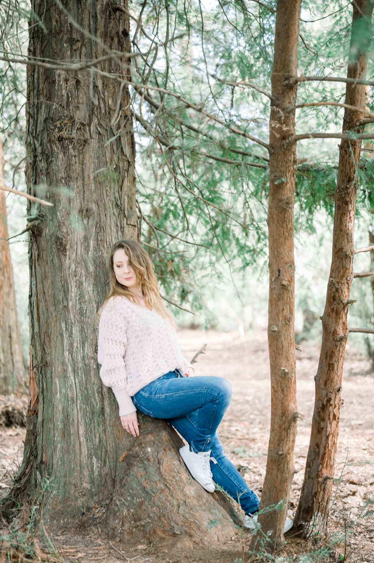 The sister sitting on a stump, leaning back against a tree trunk