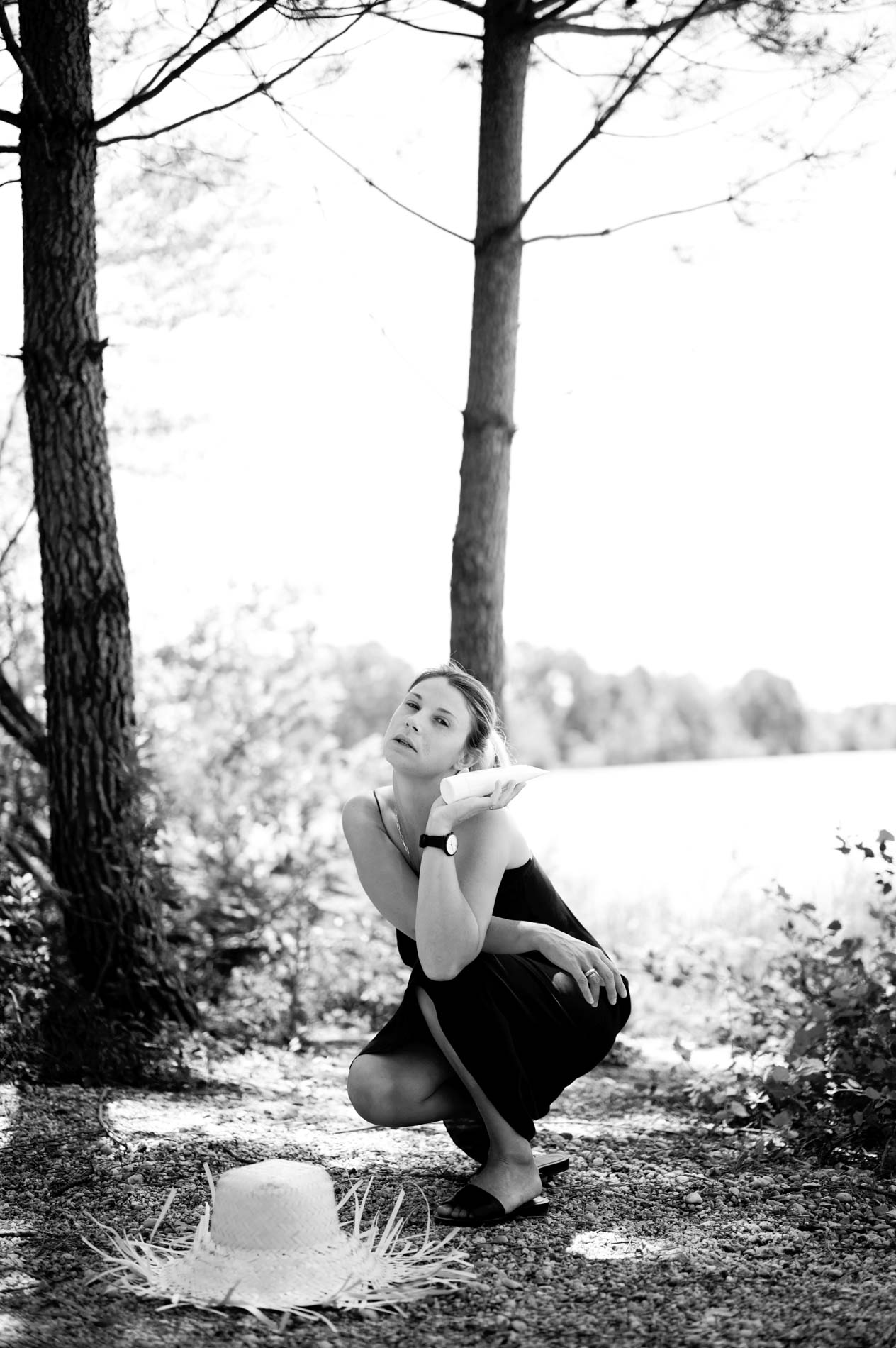 Model crouching by the water, straw hat on the ground, black and white