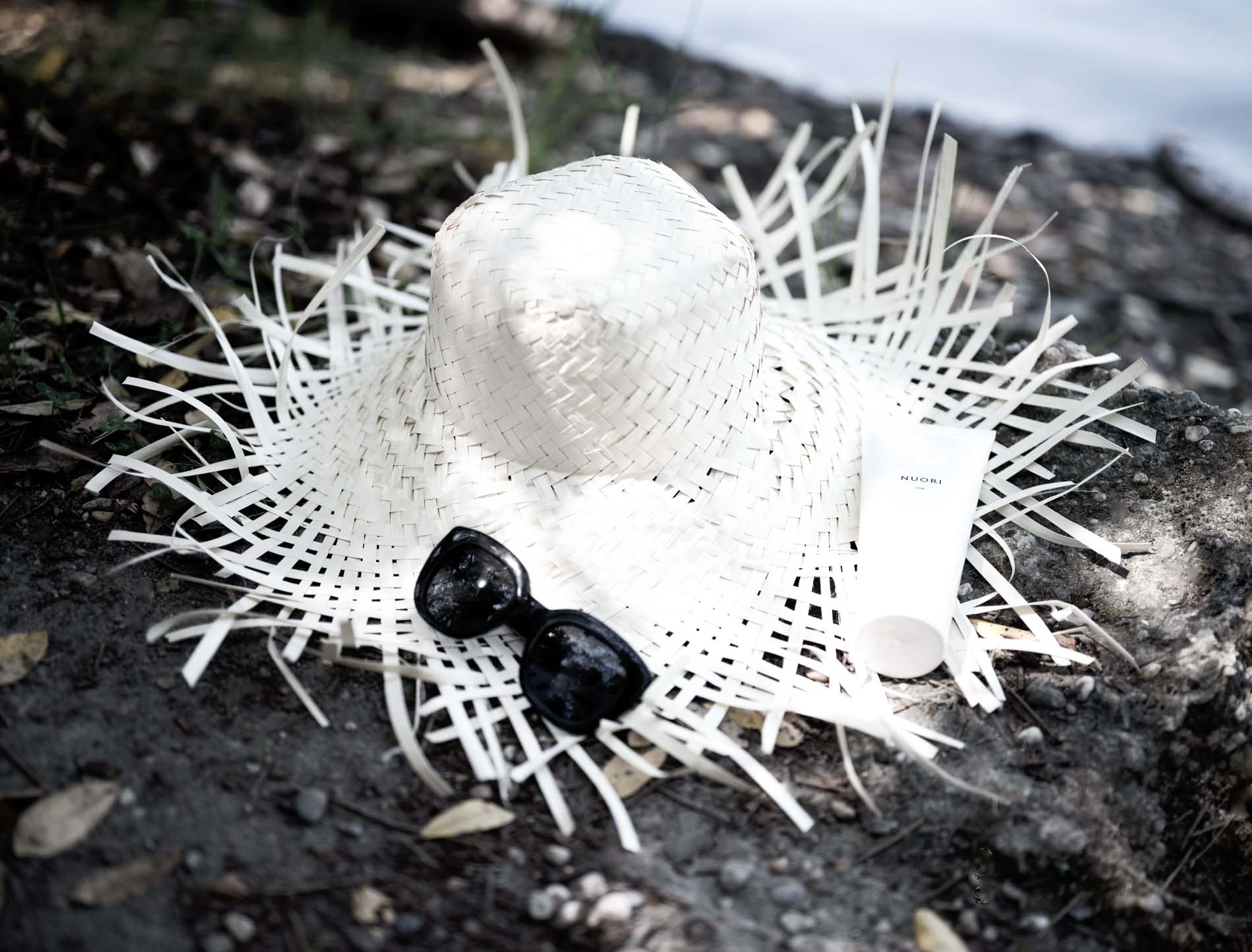 Straw hat, sunglasses and Nuori cream lying on the ground