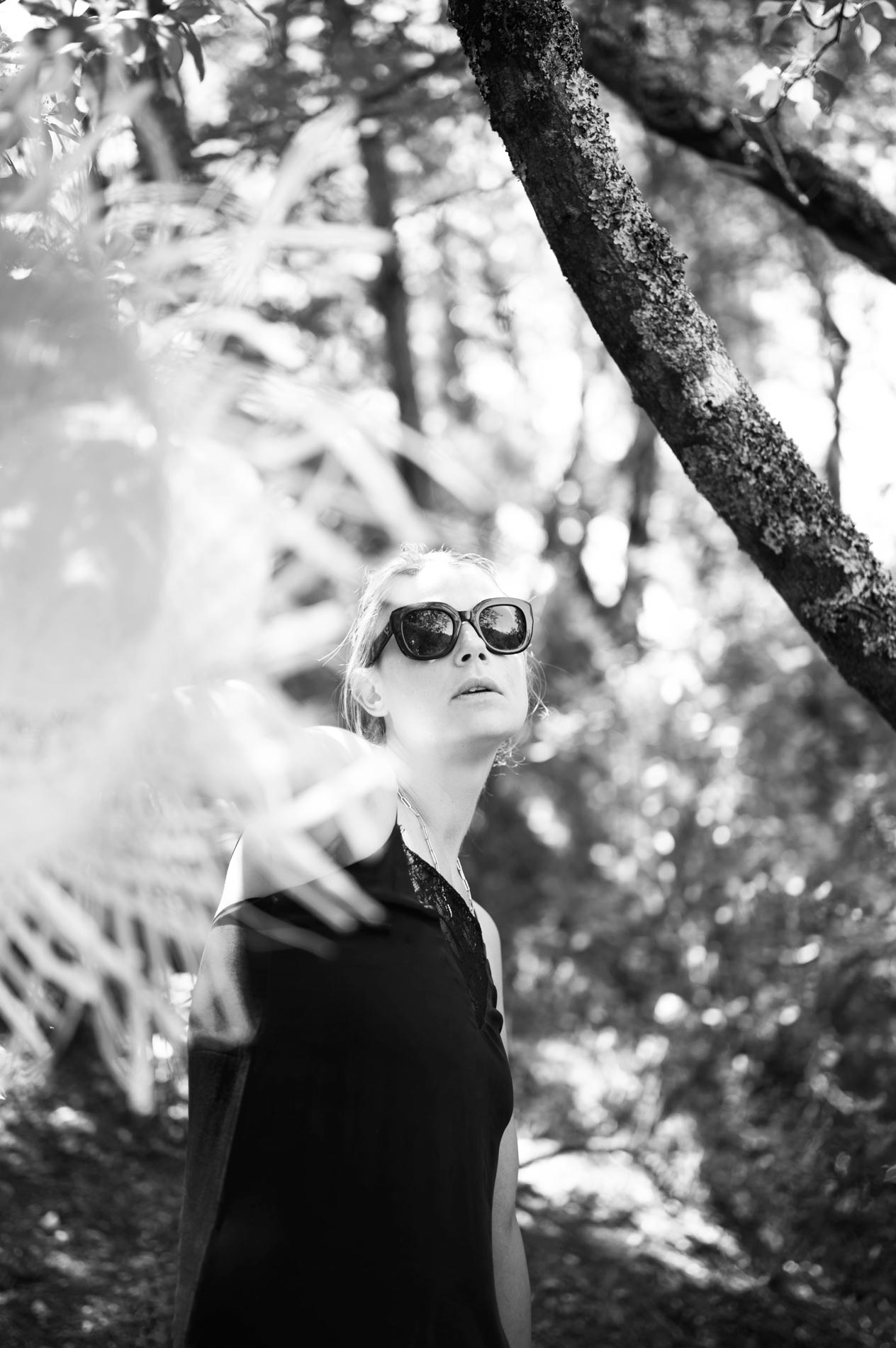 Model in sunglasses and a black top beneath the trees, black and white