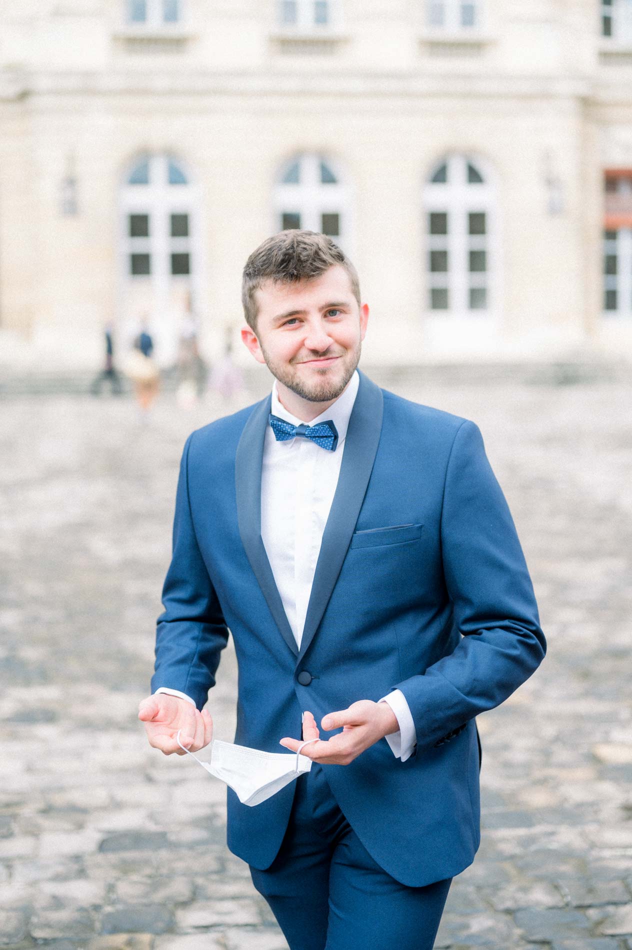 Smiling groom in a blue suit and bow tie in the city hall courtyard