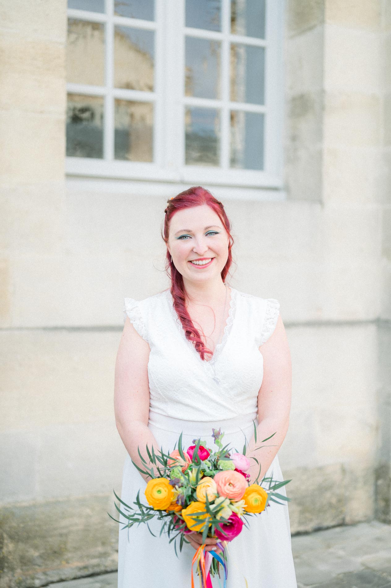 Bride with braided red hair holding a colourful bouquet outside city hall