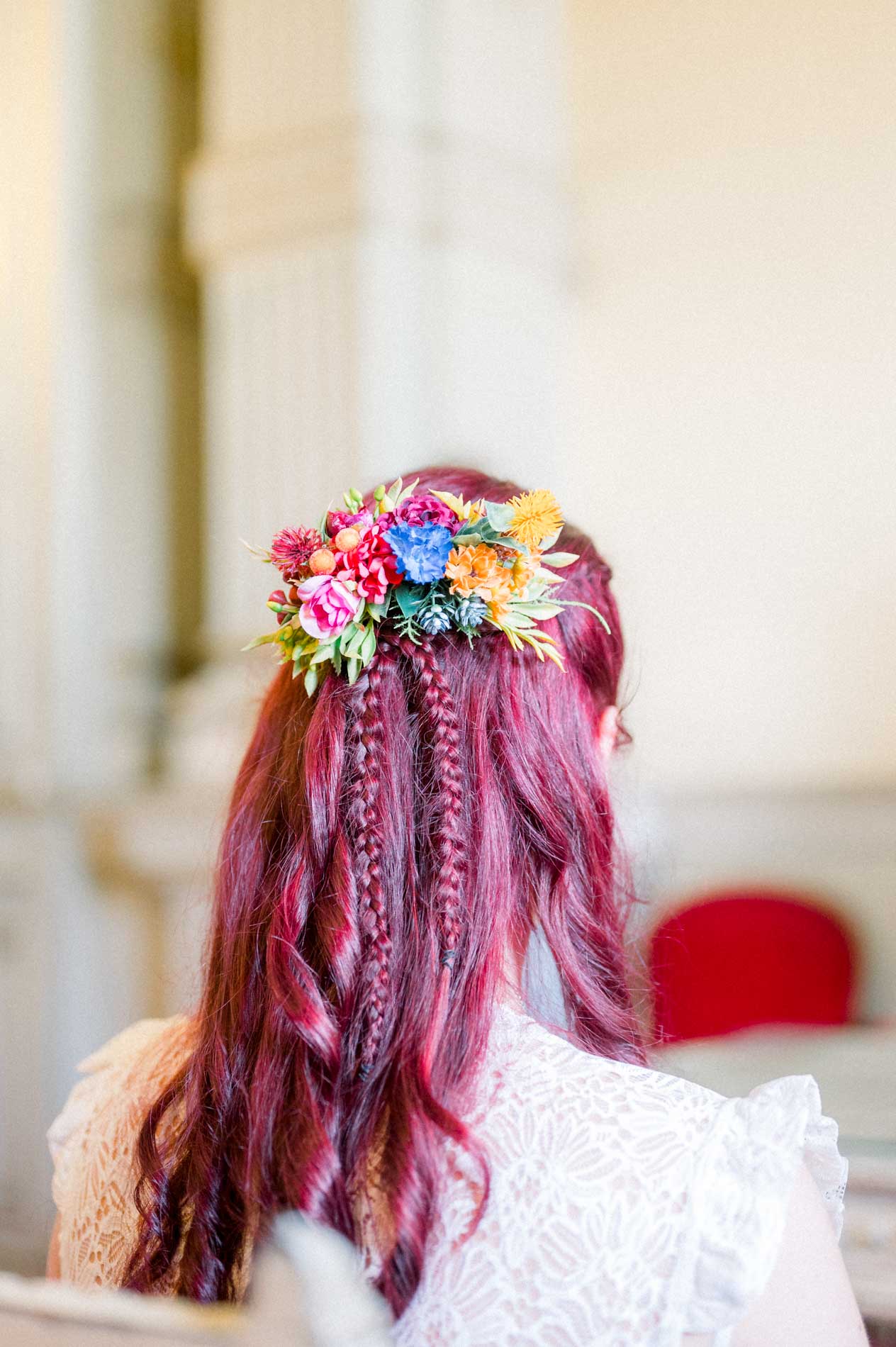 Bride's braided hairstyle adorned with colourful flowers, seen from behind