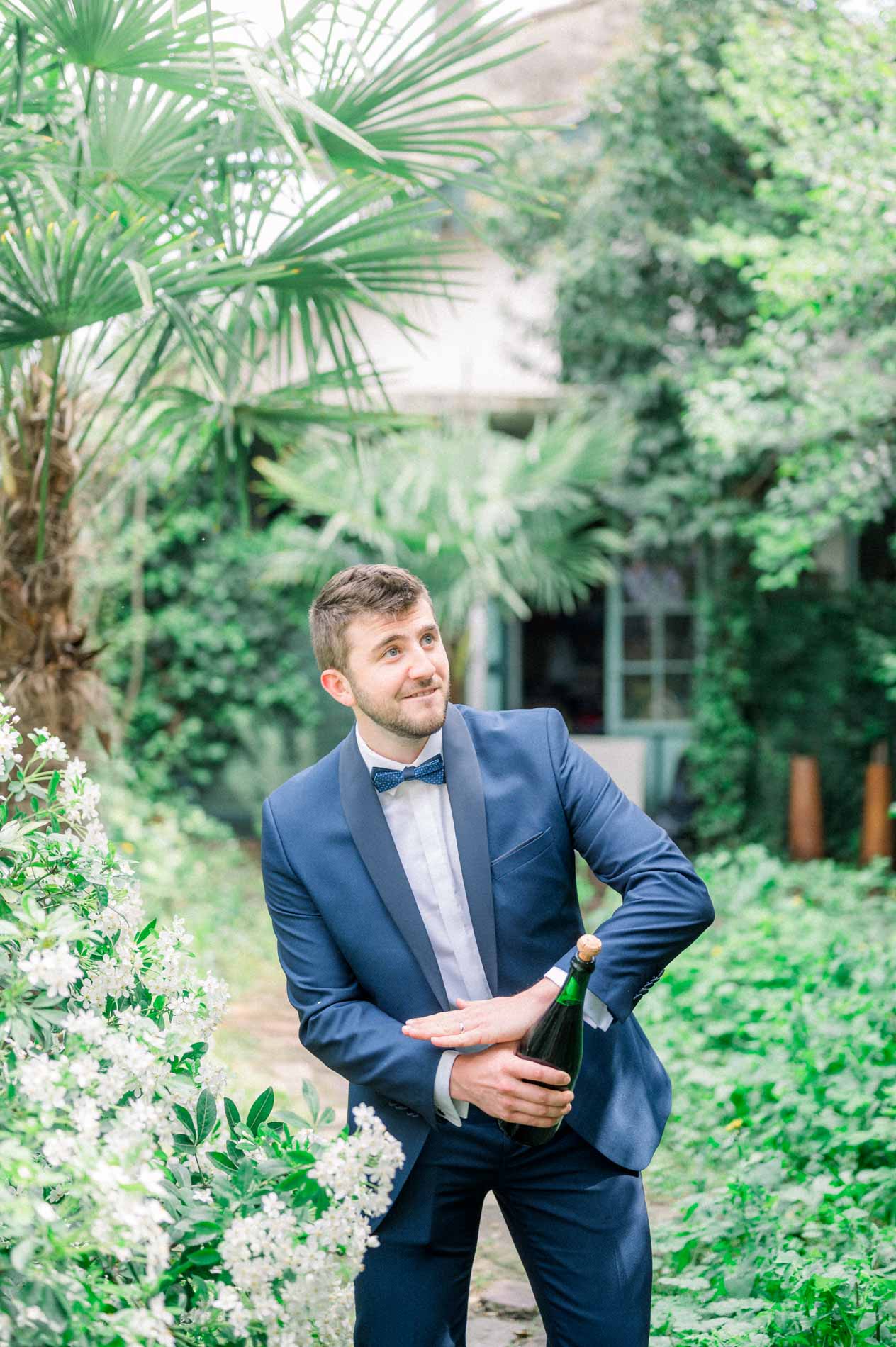 Groom popping a bottle of champagne in a lush garden