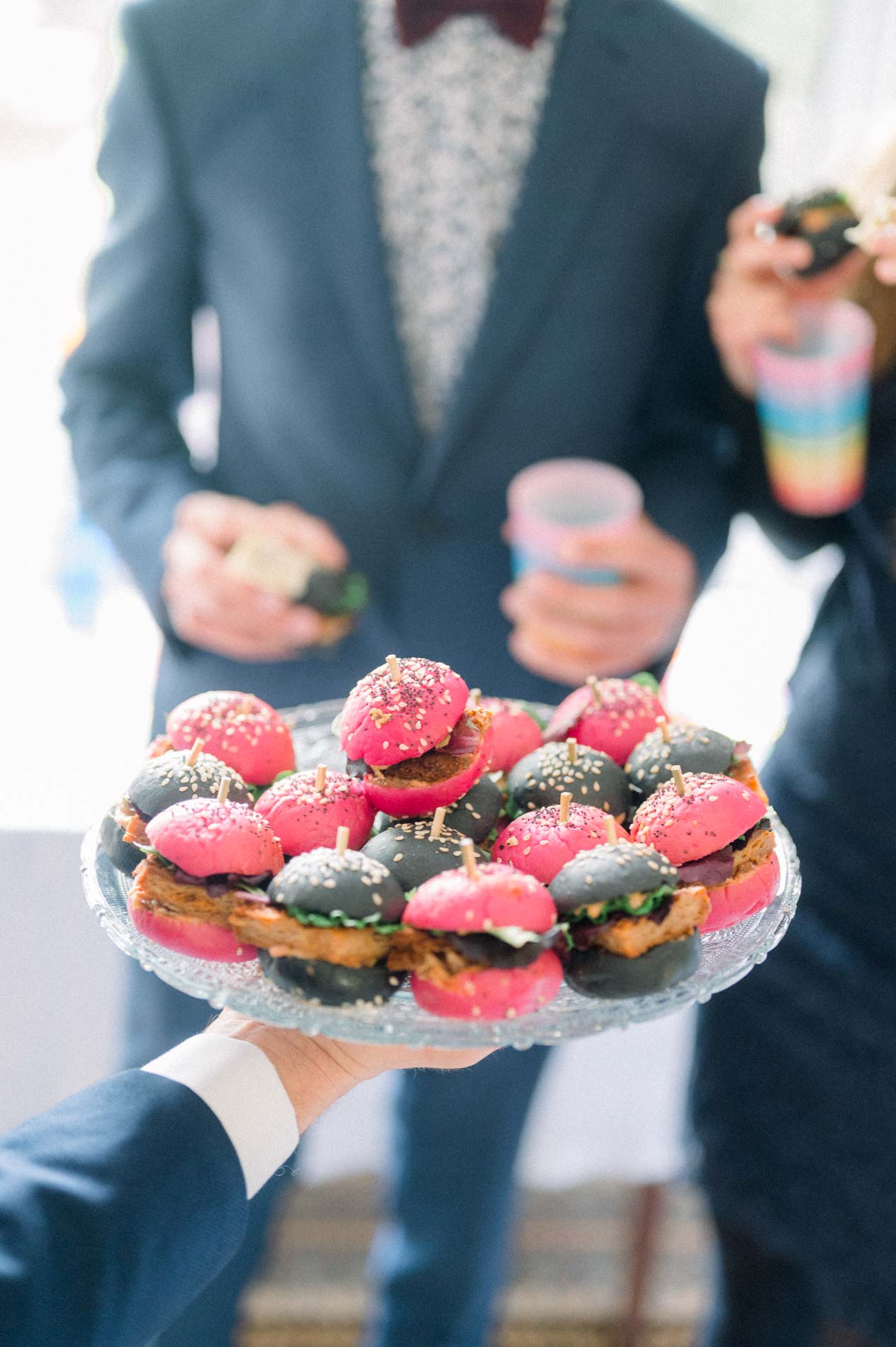 Tray of vegan mini sandwiches on pink buns held by a guest