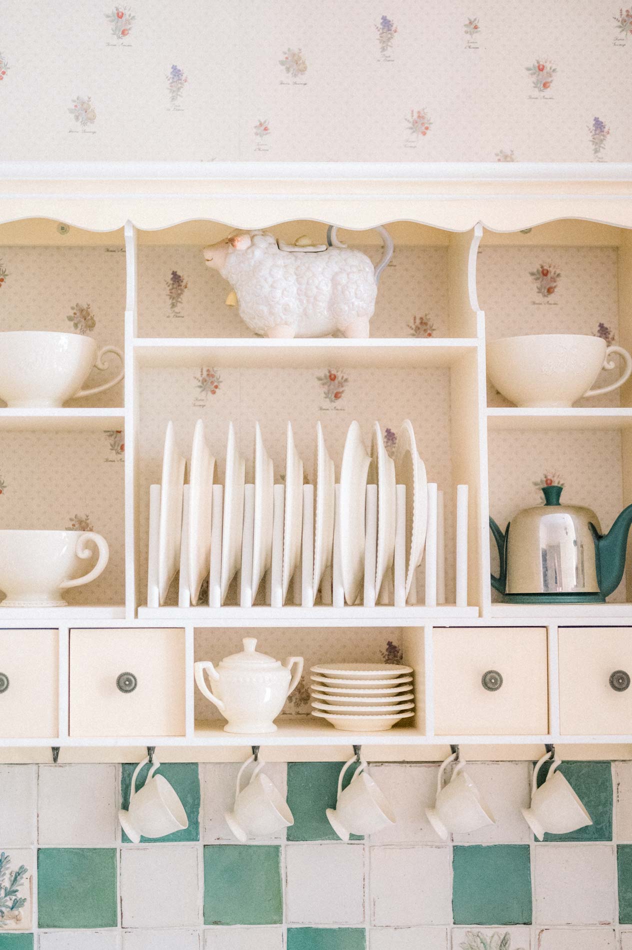White dresser lined with cups and plates above green tiles