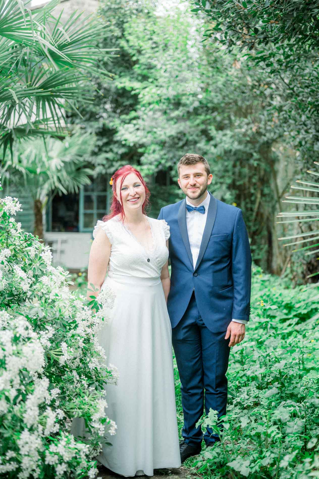 Bride and groom standing among palms and white blossoms in the garden