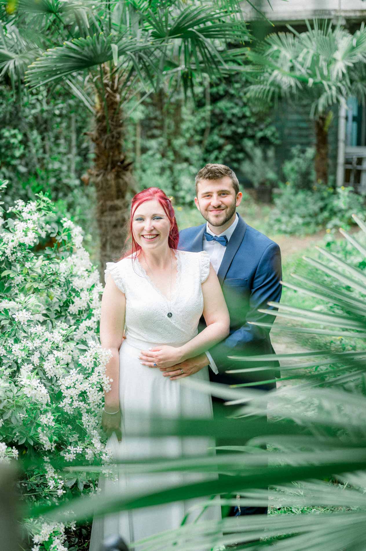 Bride and groom embracing behind palm fronds in the foreground