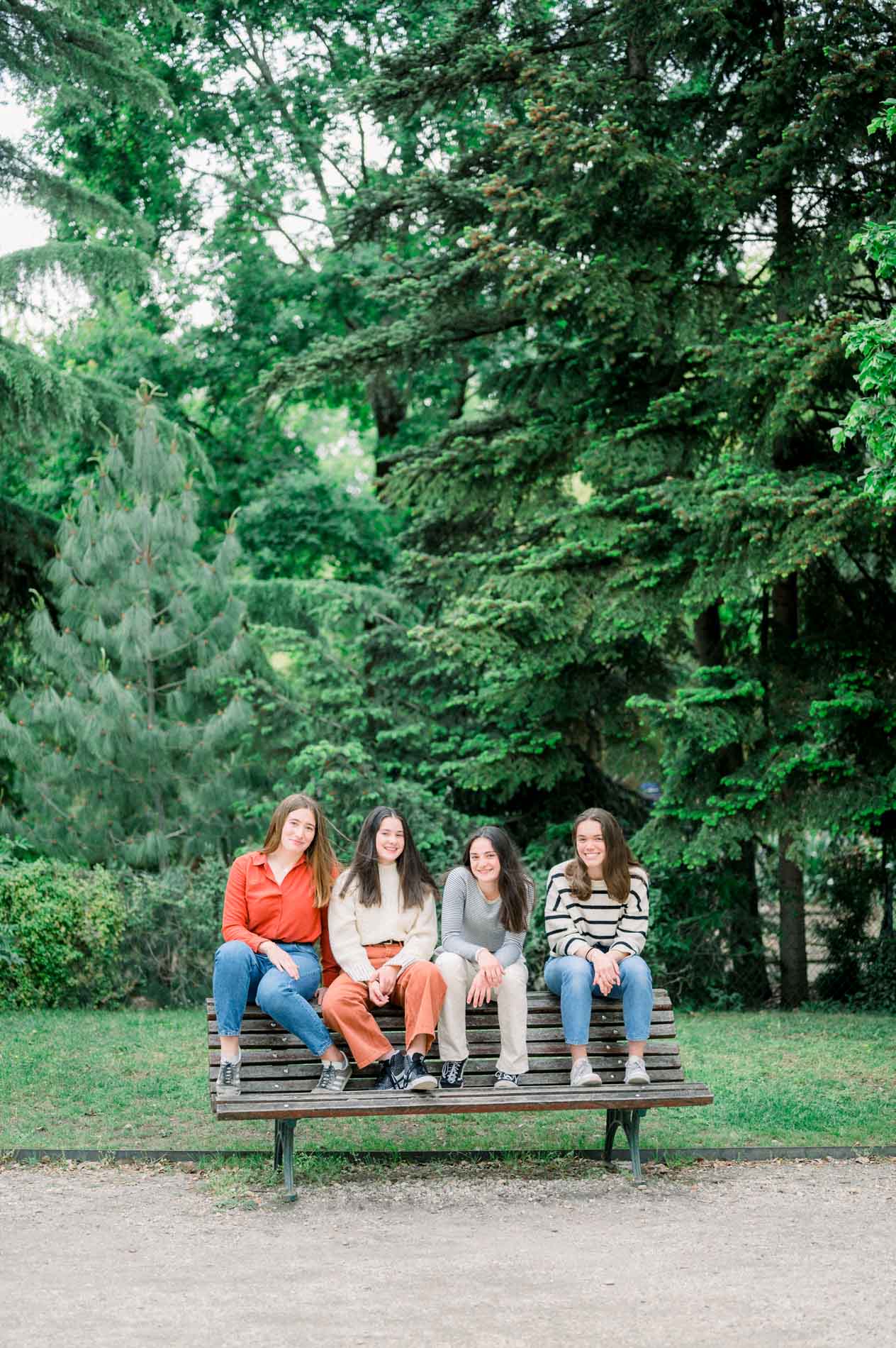 Quatre amies assises sur un banc en bois sous les grands arbres du Jardin Public