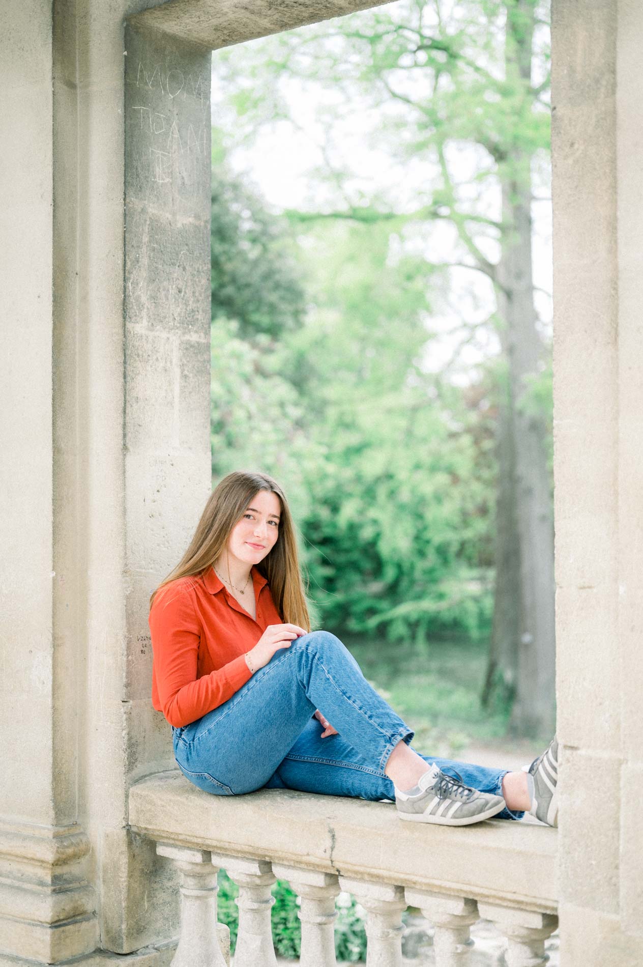 Jeune femme en chemise orange assise sur une balustrade entre deux piliers