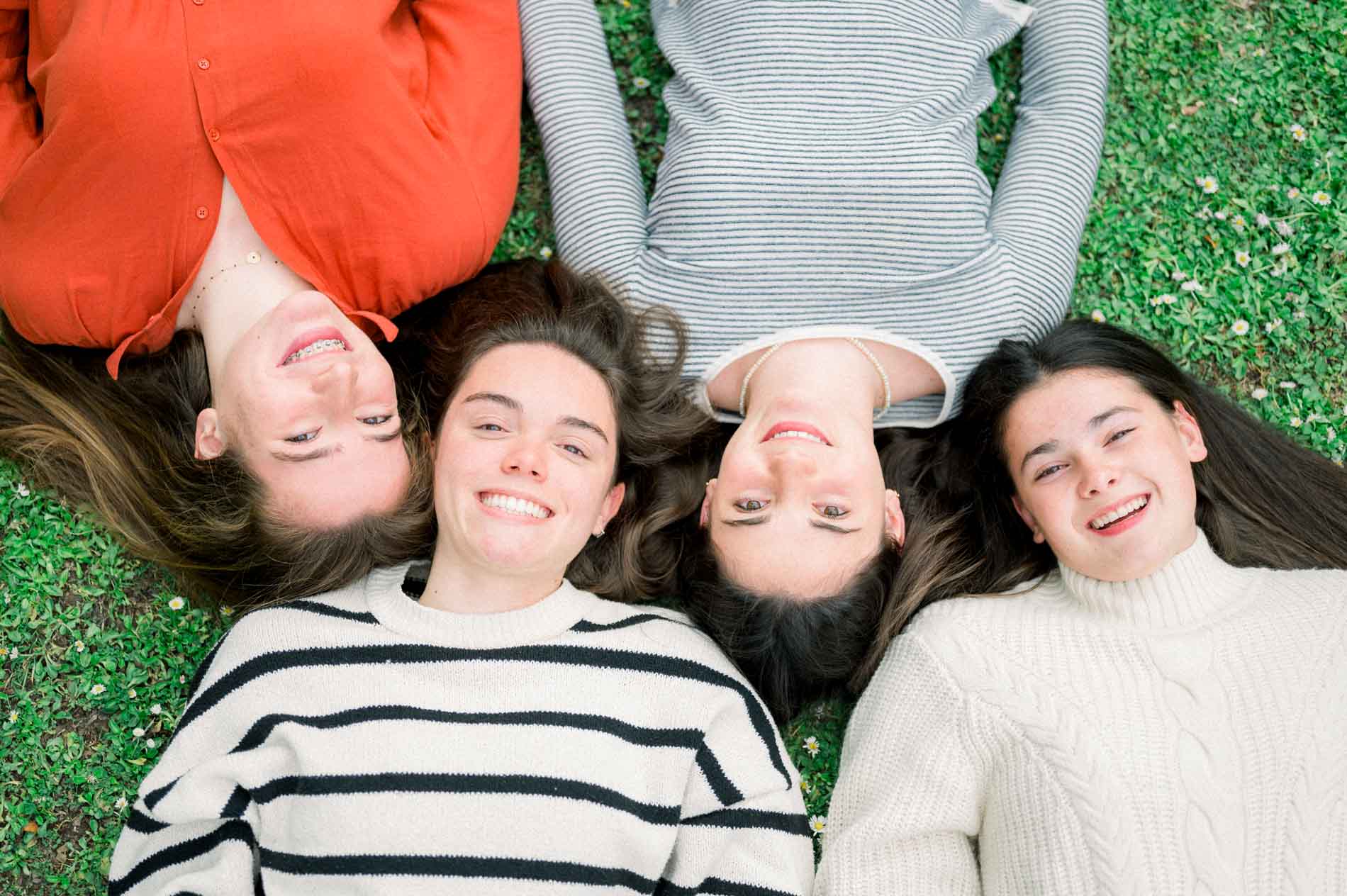 Quatre amies allongées dans l'herbe, têtes rapprochées, éclatant de rire