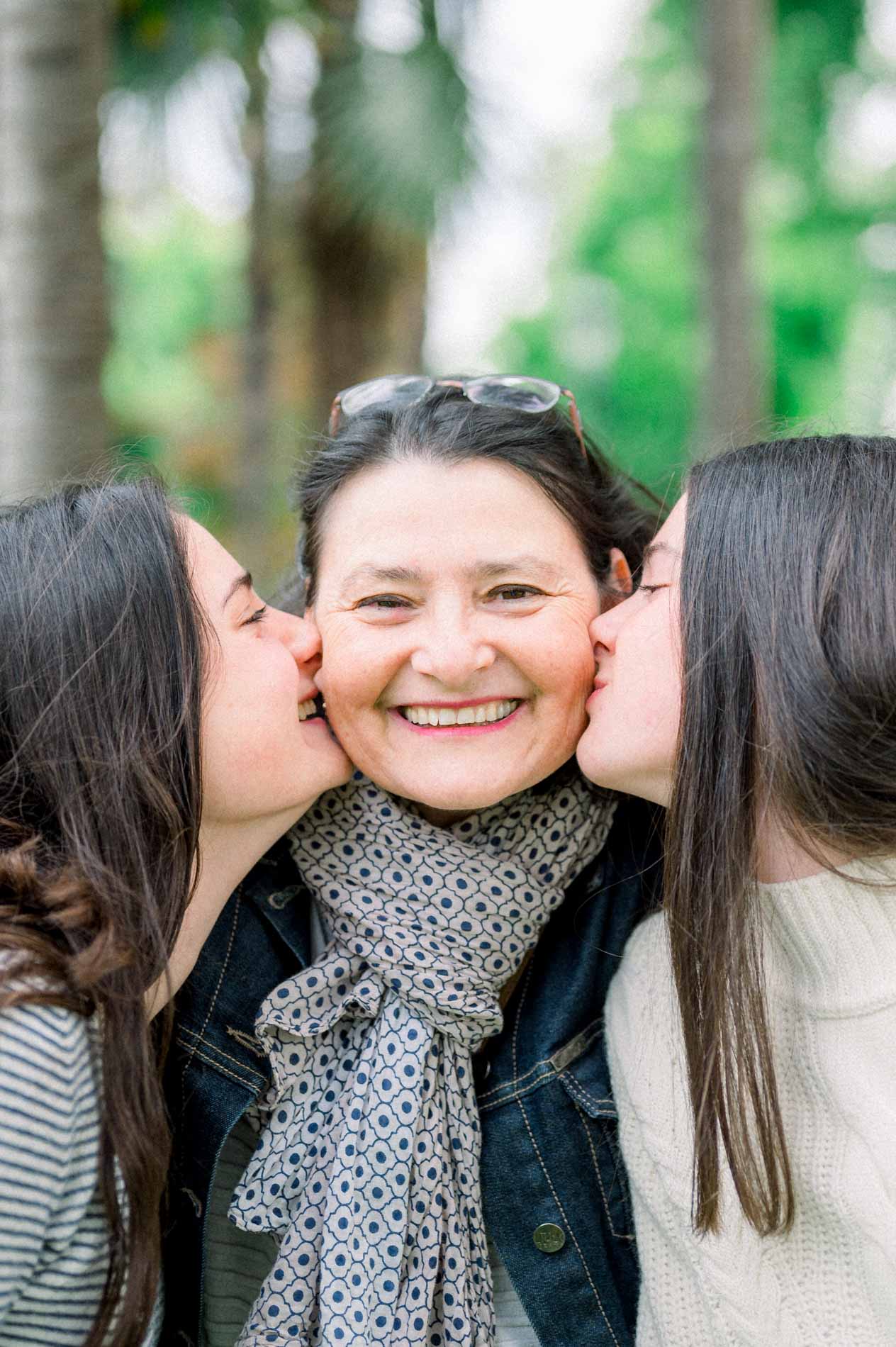 Deux jeunes femmes embrassent les joues d'une femme souriante, séance en famille