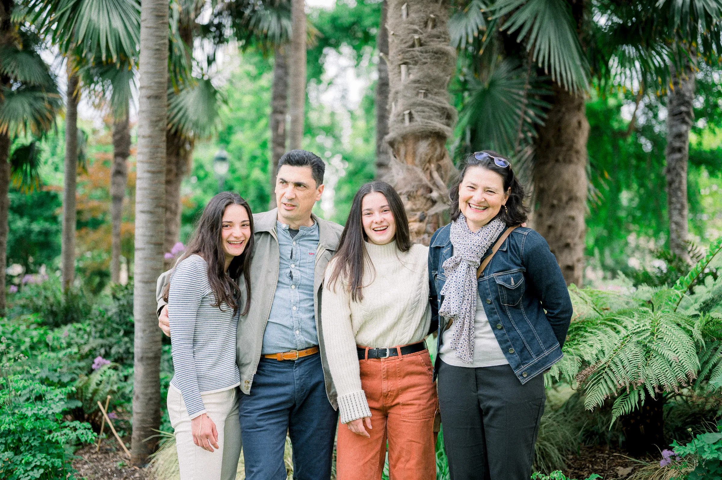 Famille souriante serrée devant les palmiers et les fougères du jardin