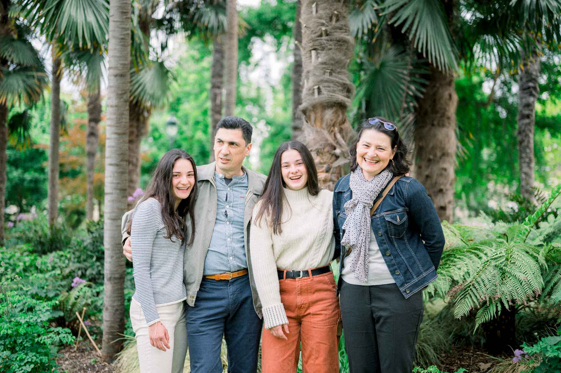 Famille souriante serrée devant les palmiers et les fougères du jardin