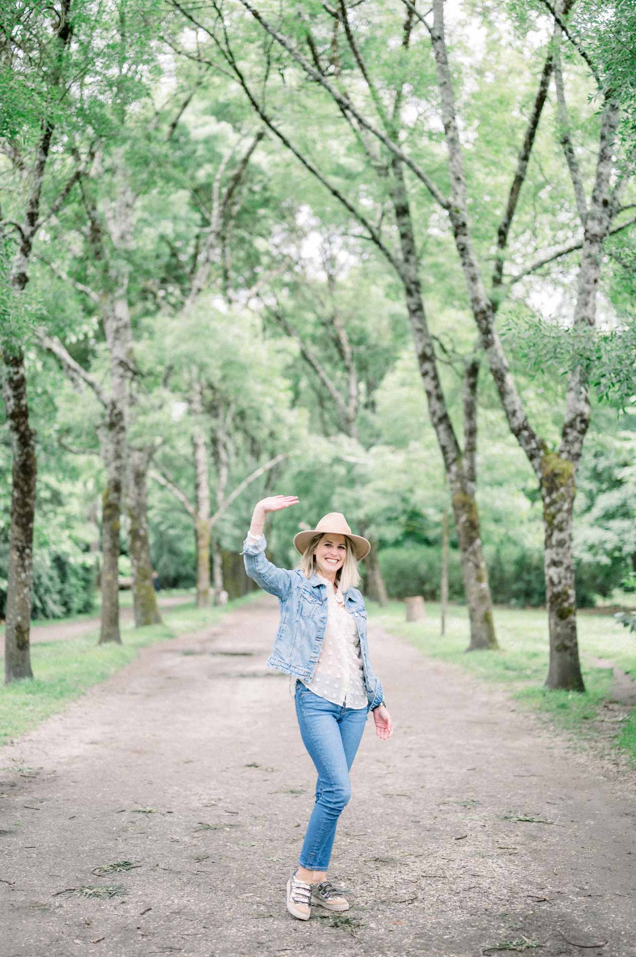 The mother dancing with her hat in hand along a tree-lined path