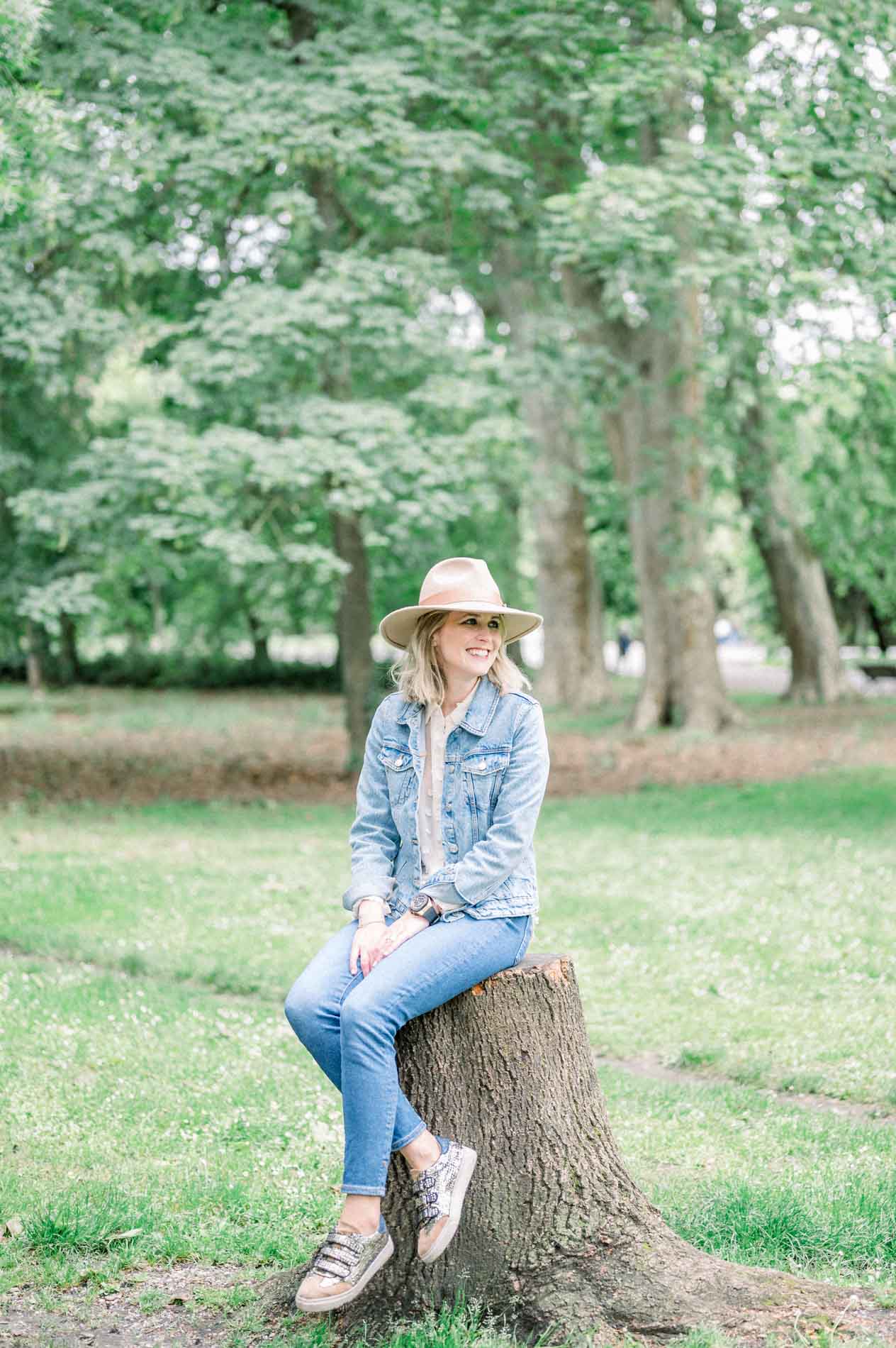 The mother in a hat and denim jacket sitting on a tree stump in the park