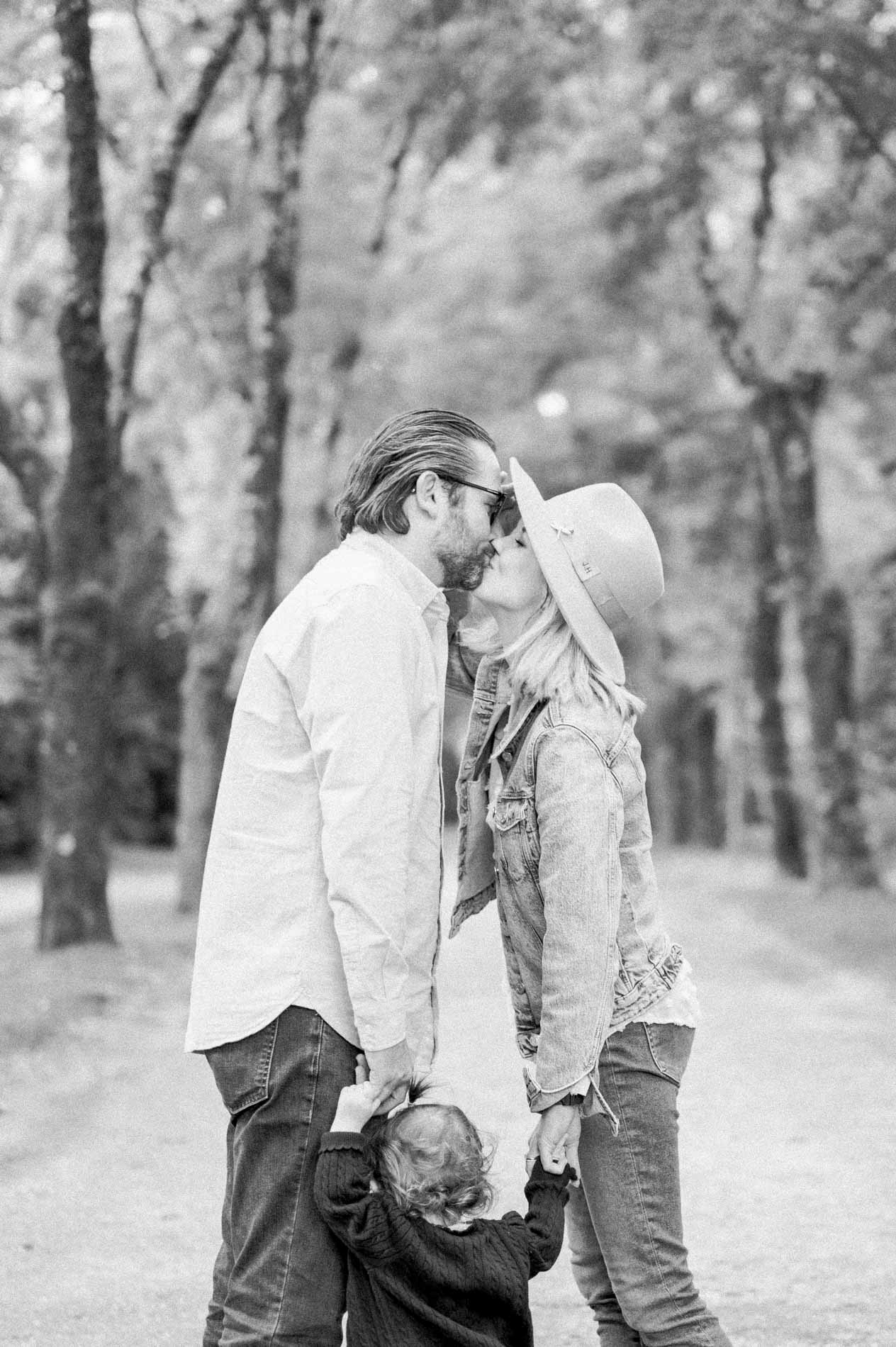 The parents kiss as their little girl clings to them, in black and white