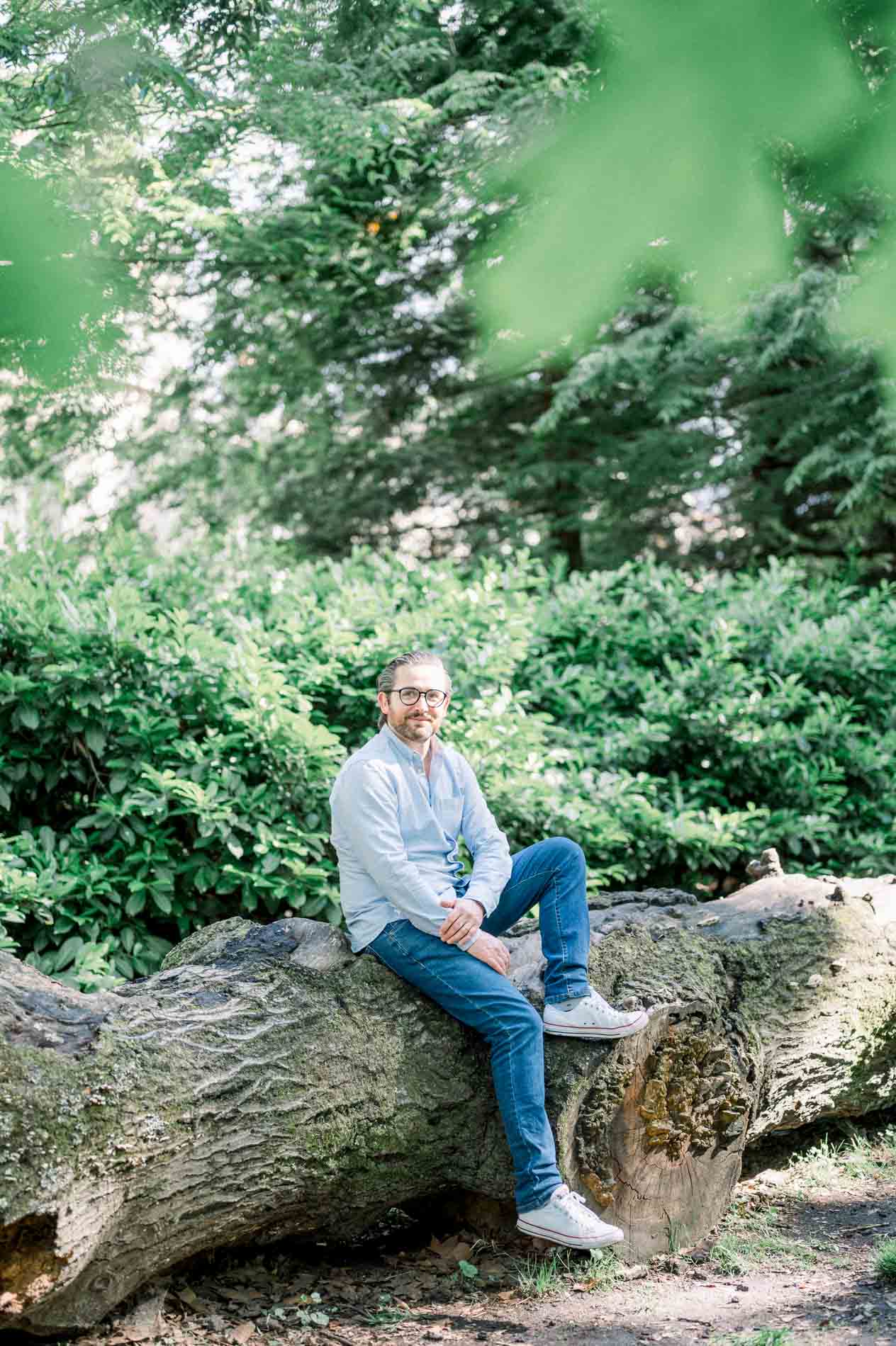 The father in a blue shirt sitting on a large fallen trunk
