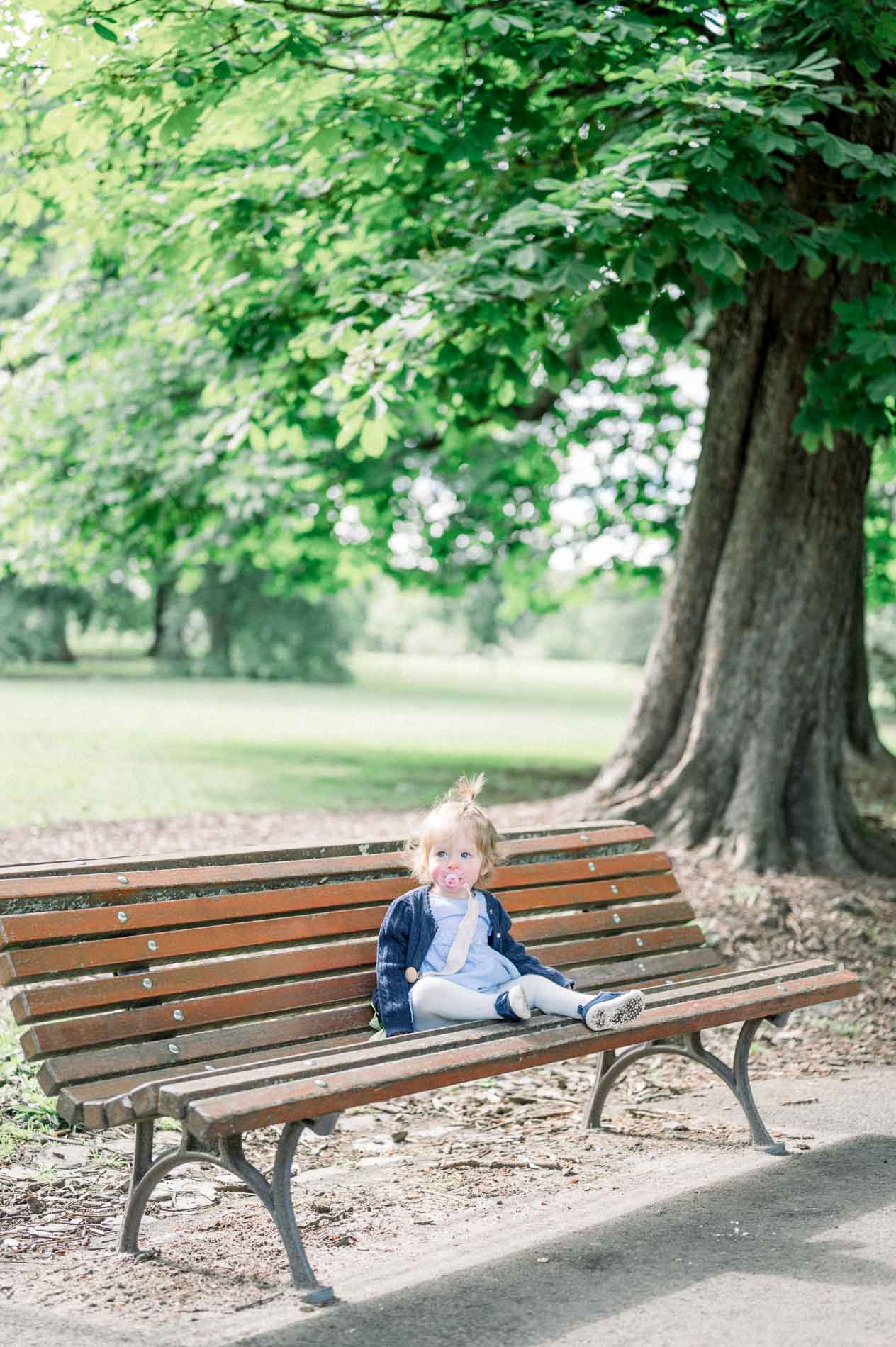 The little girl sitting alone on a wooden bench under a chestnut tree