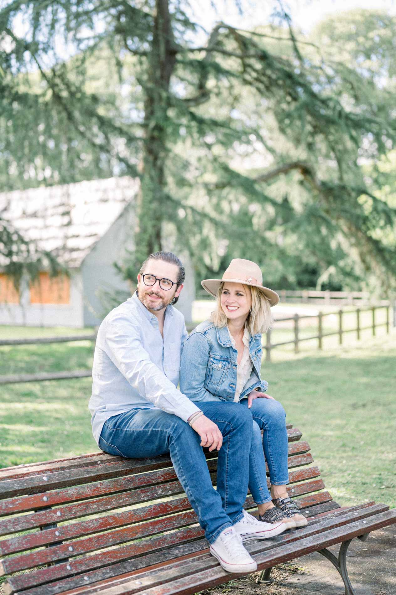 The parents sitting on the back of a bench in front of a wooden park building