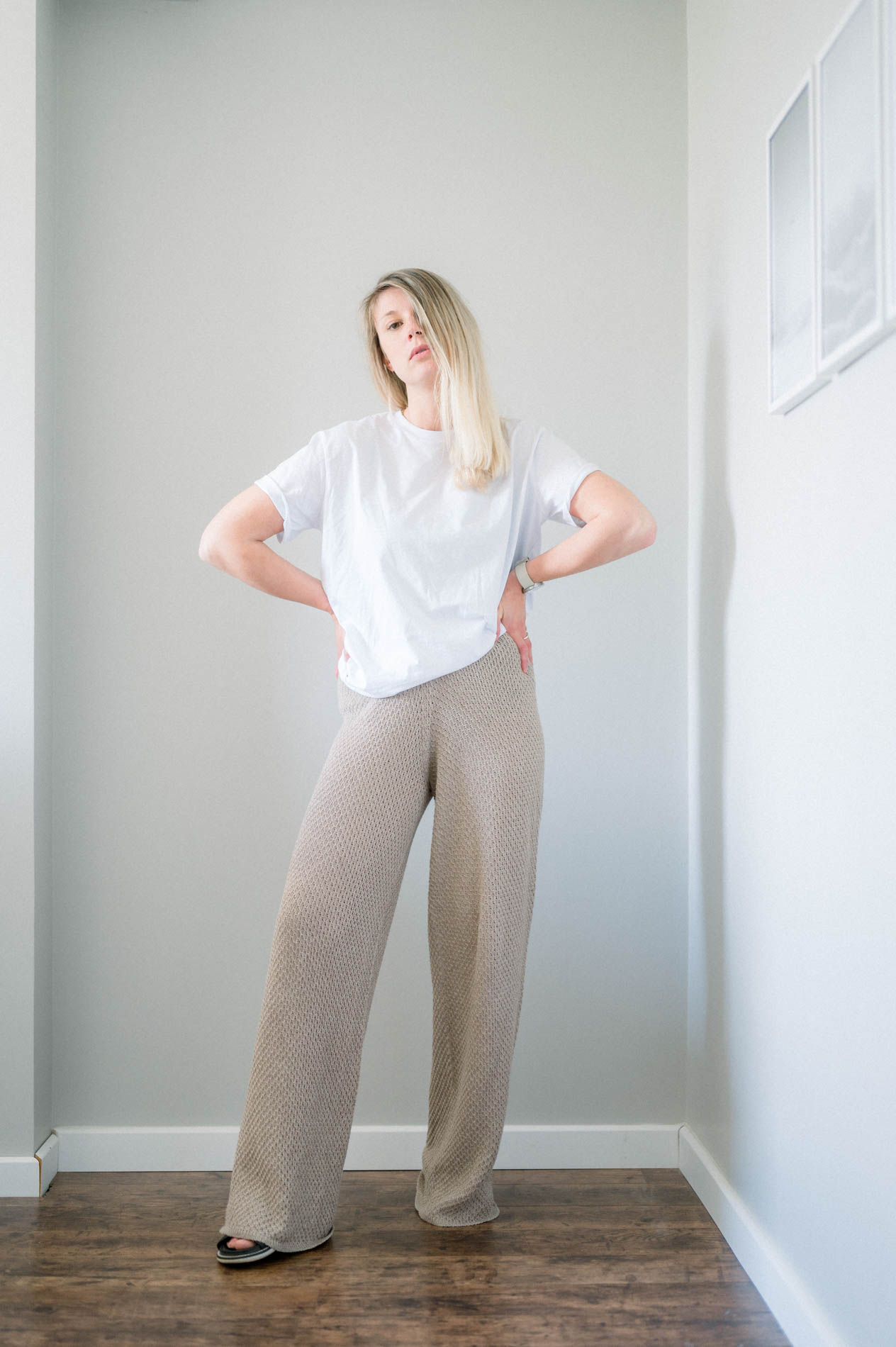 Model in a white T-shirt and wide beige trousers, hands on hips