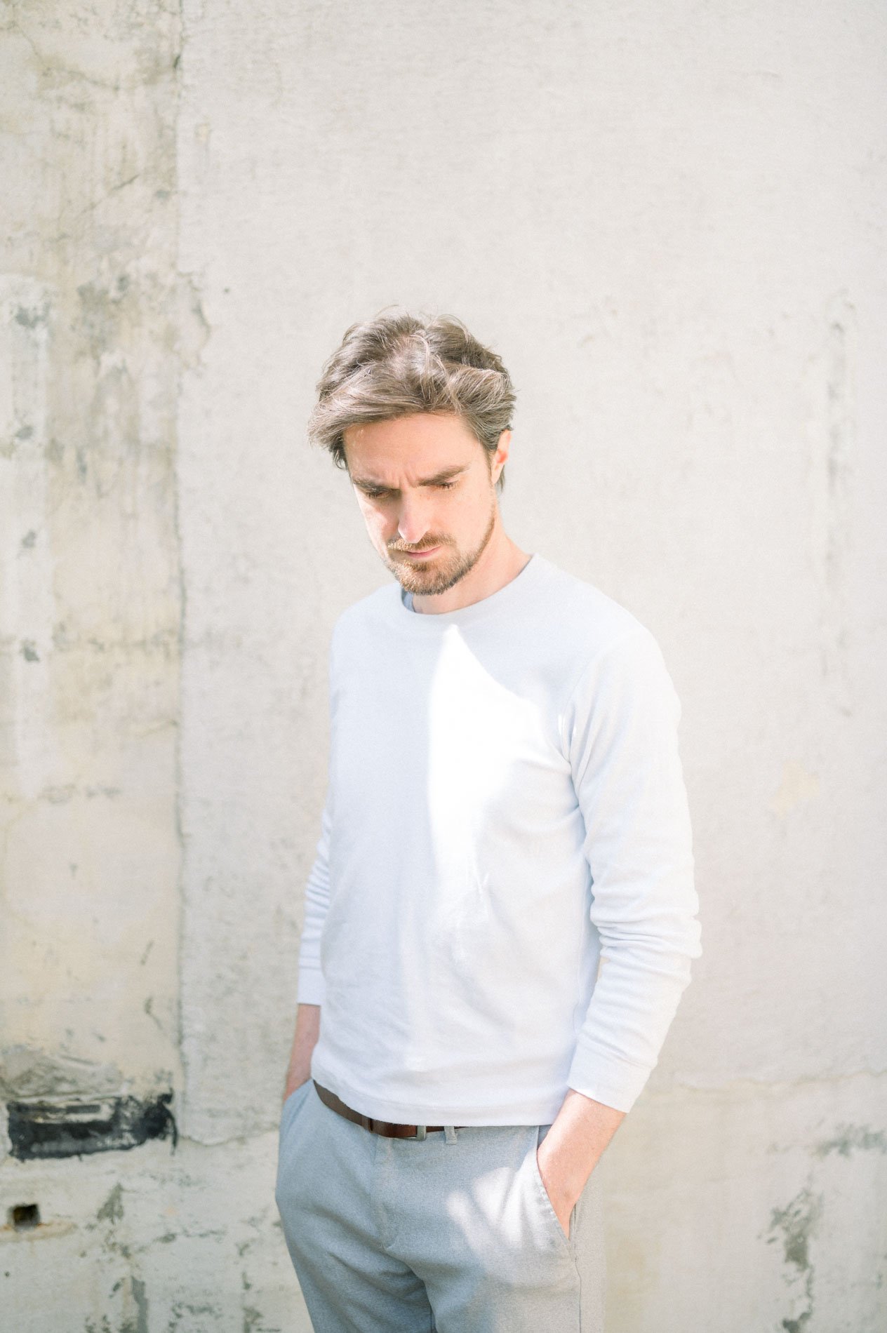 Male model in a white jumper against a raw wall, Linesmanner fashion shoot