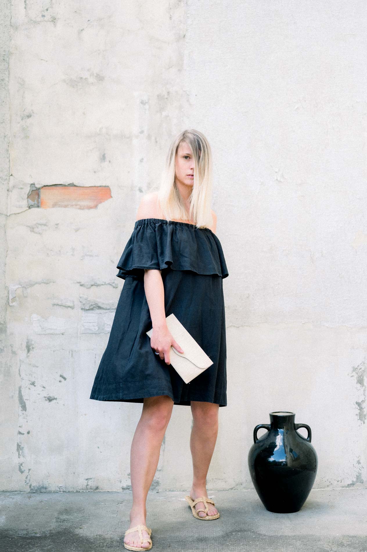 Model in an off-the-shoulder black dress beside a ceramic jar