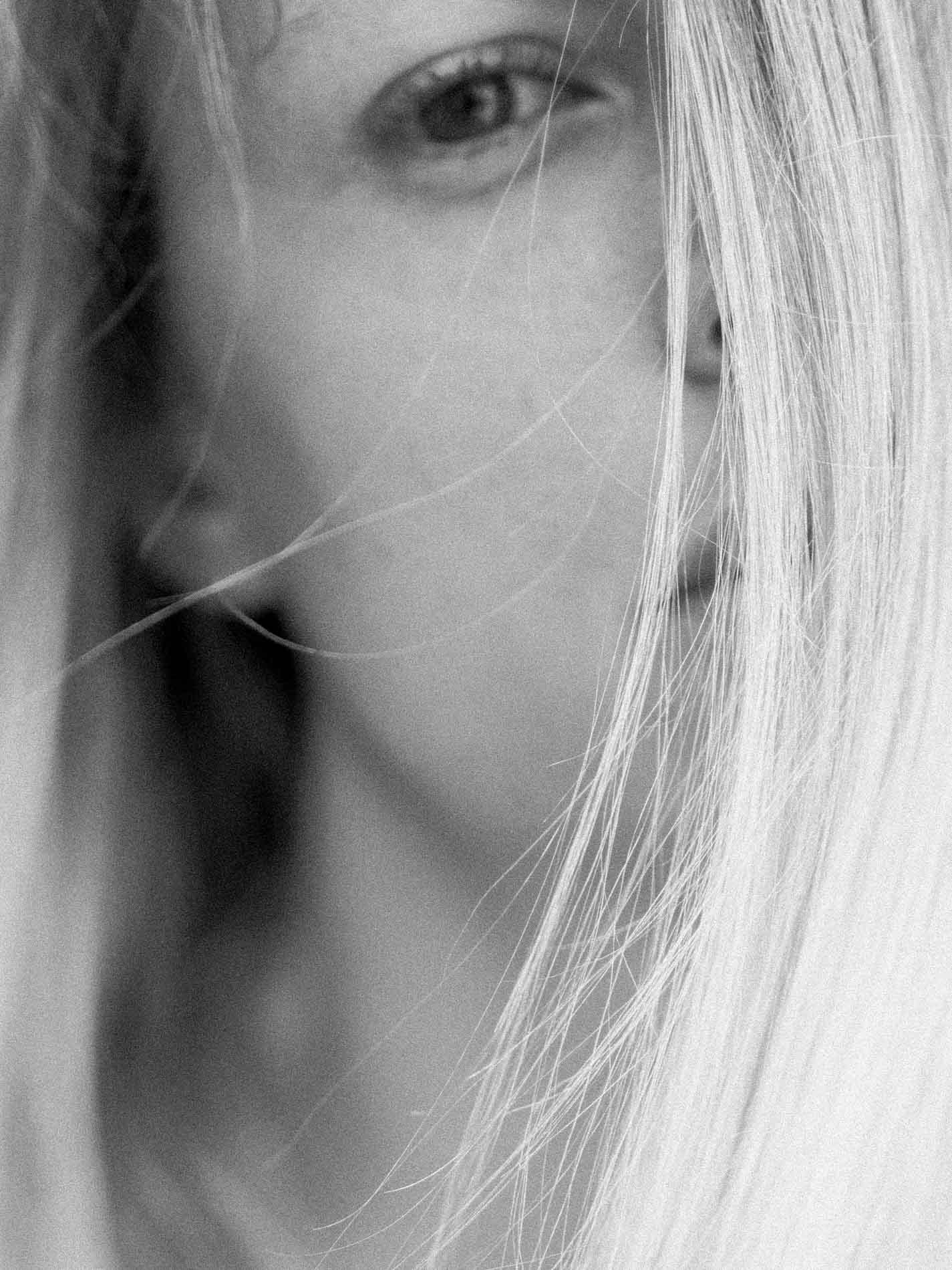 Close-up of a blonde model's gaze, hair across her face, black and white