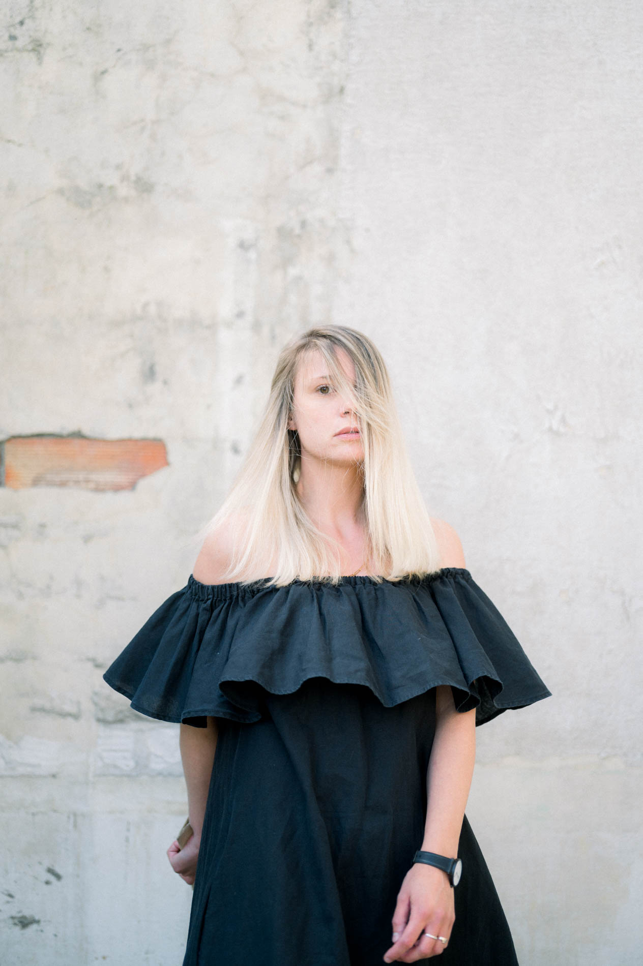 Blonde model in a ruffled black dress against a stone wall