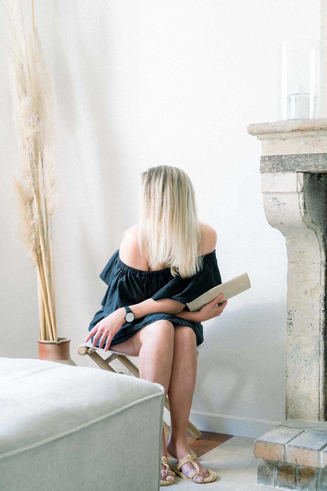 Model sitting by a stone fireplace reading a book