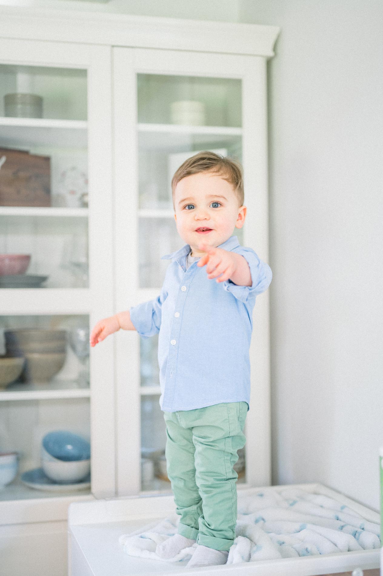 Toddler in a blue shirt standing on a pouffe, pointing