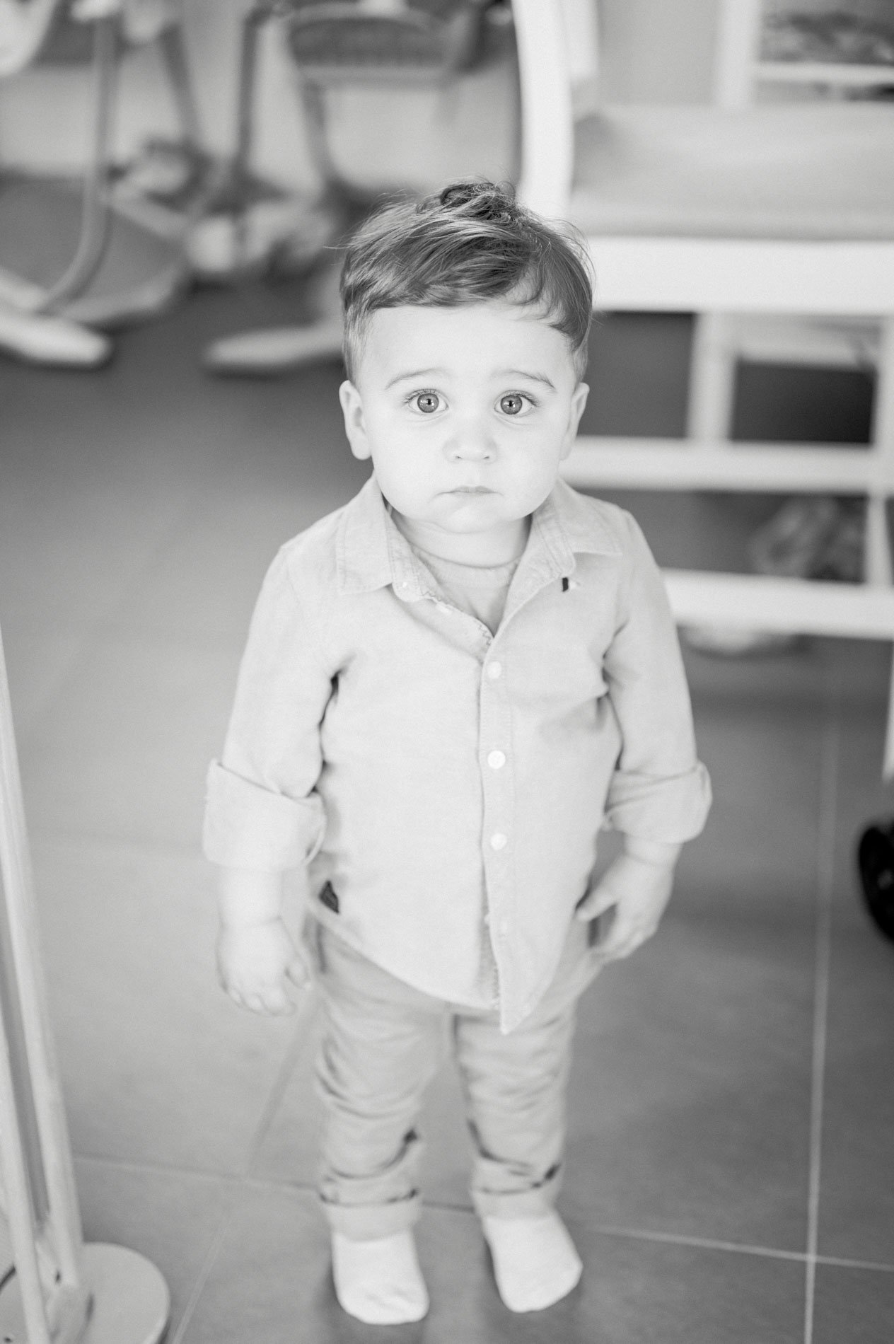 Toddler in a shirt in the kitchen, staring at the camera, in black and white