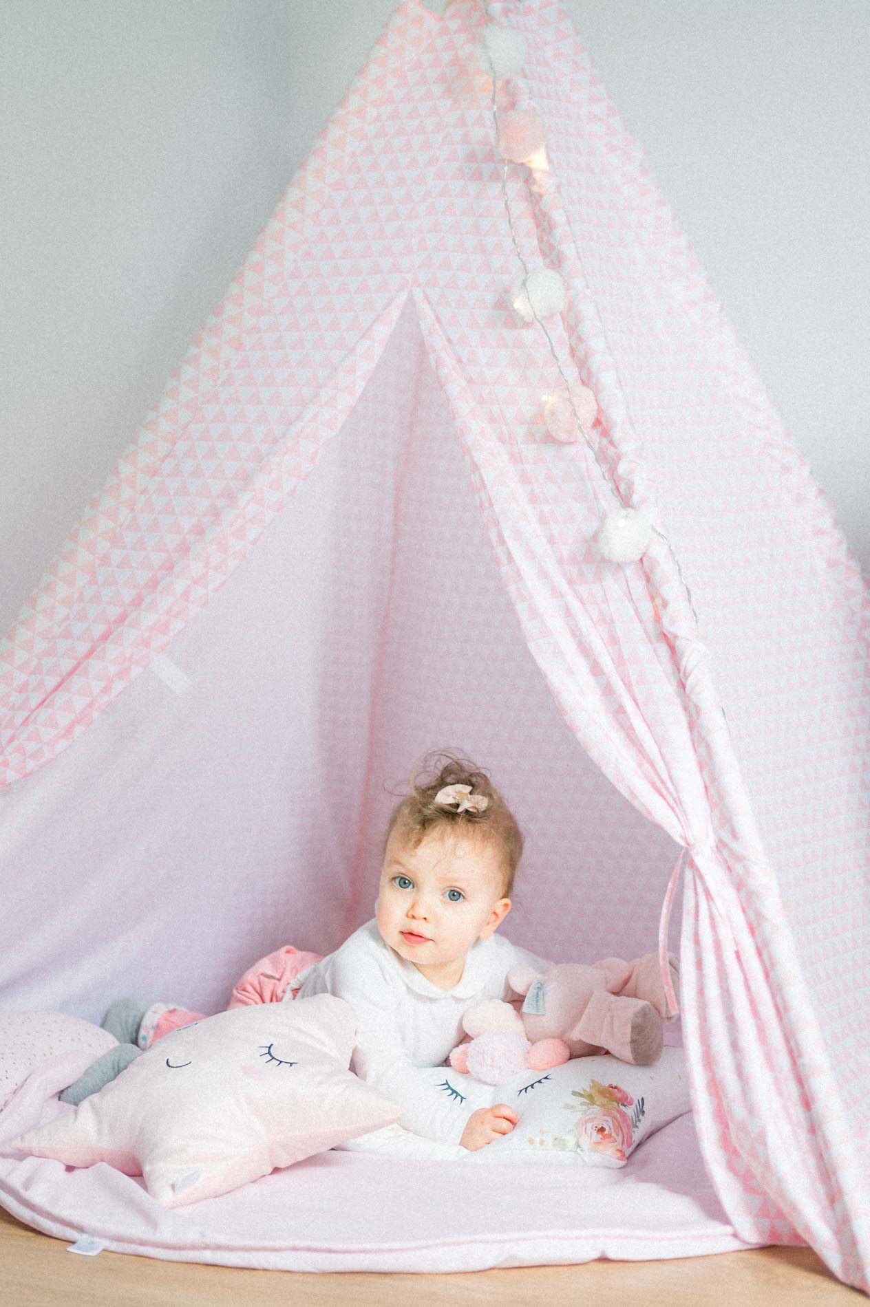 Smiling baby surrounded by cushions in a pink teepee