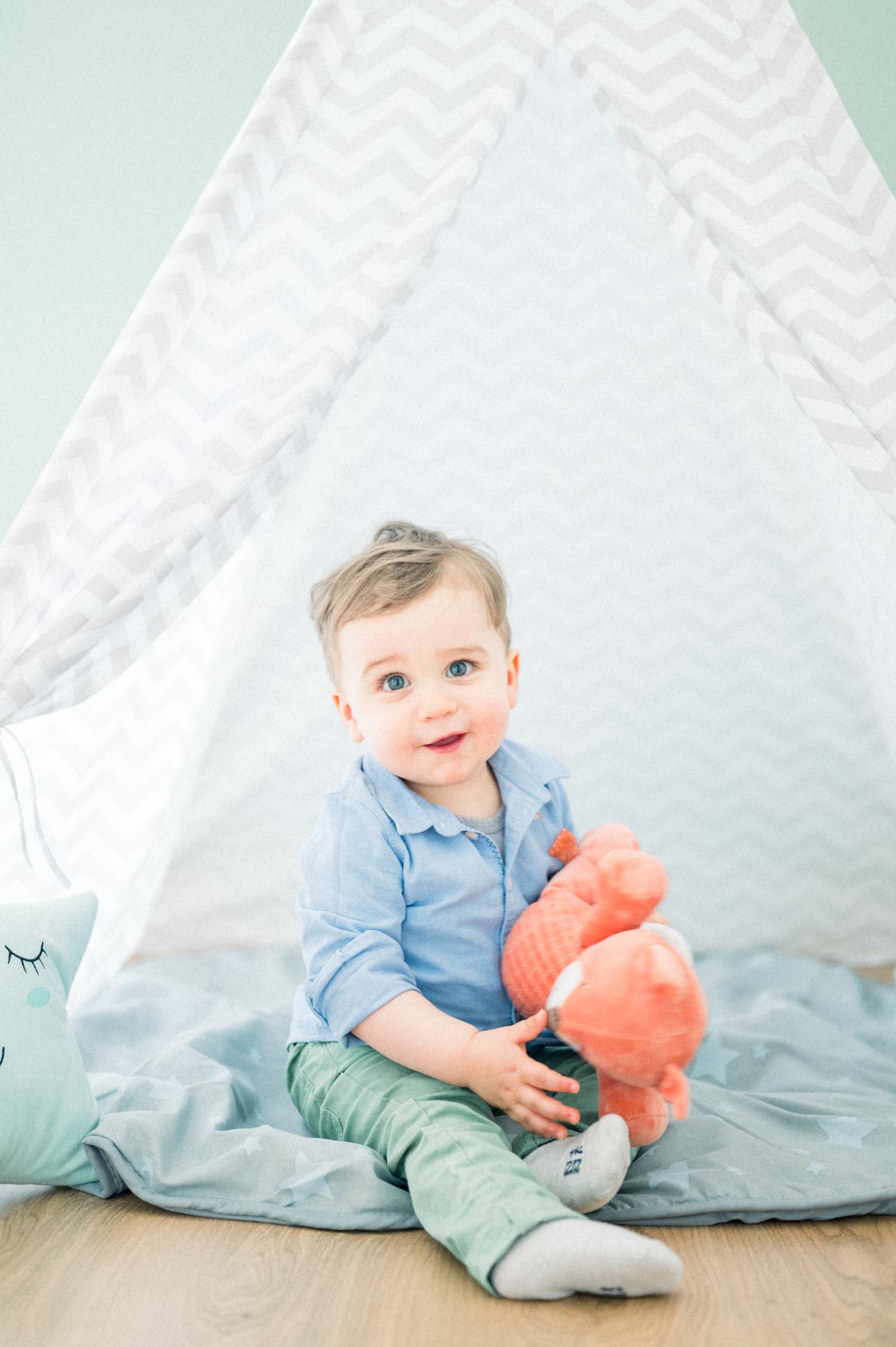 Toddler sitting in a grey teepee with a toy fox