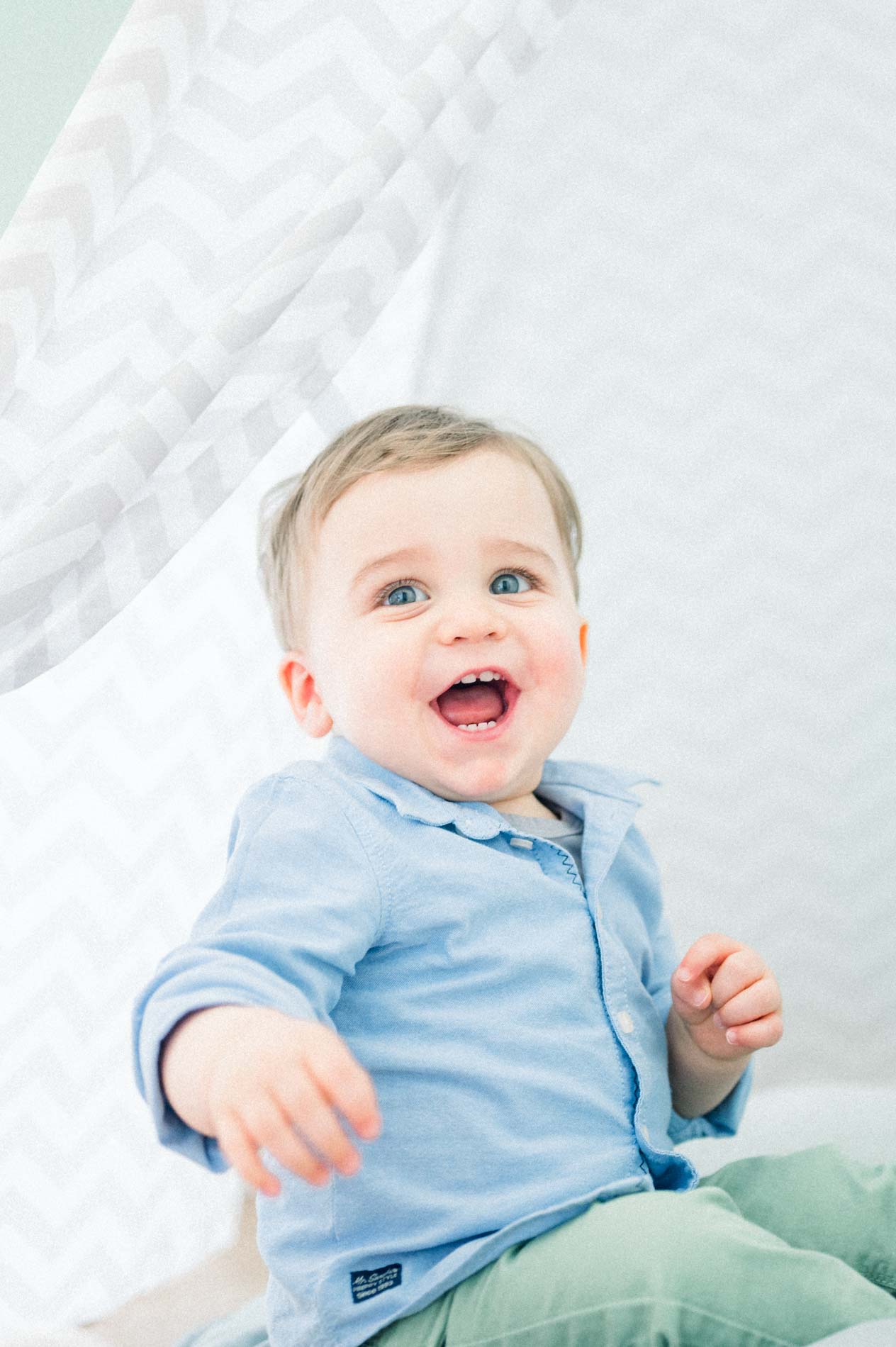Toddler bursting with laughter under the teepee in a blue shirt