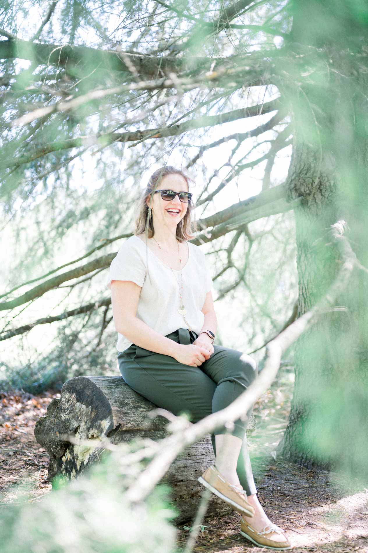 Mum in sunglasses sitting on a log beneath the pines
