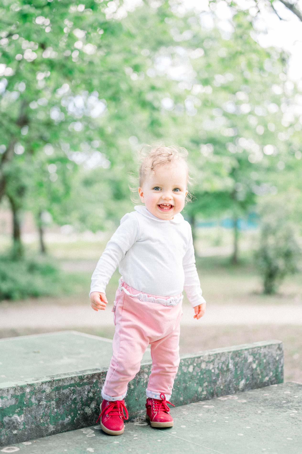 Smiling baby standing on the ping-pong table in red trainers