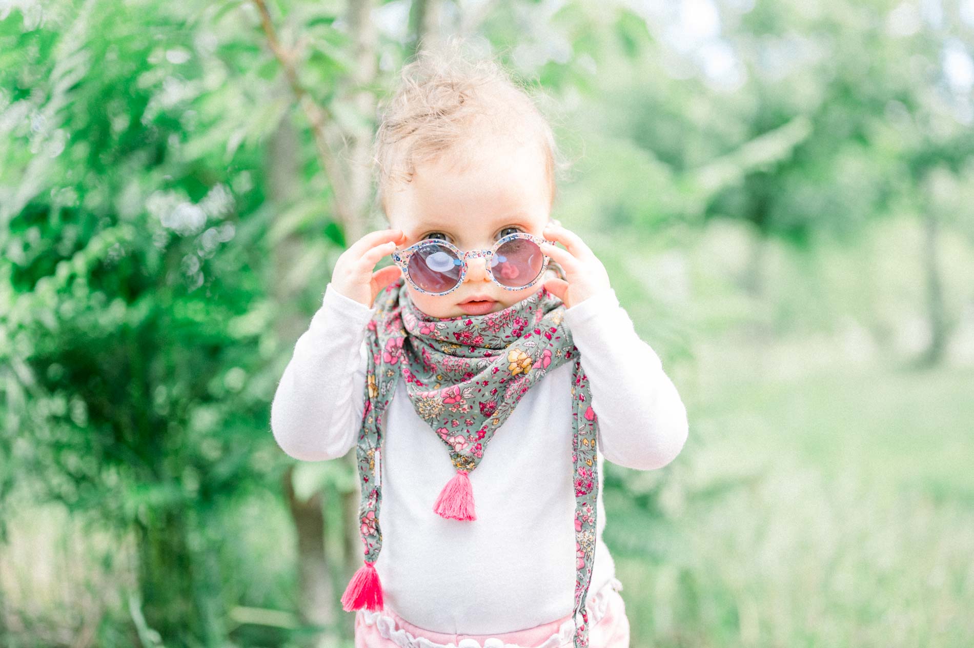 Baby in a floral scarf adjusting round sunglasses