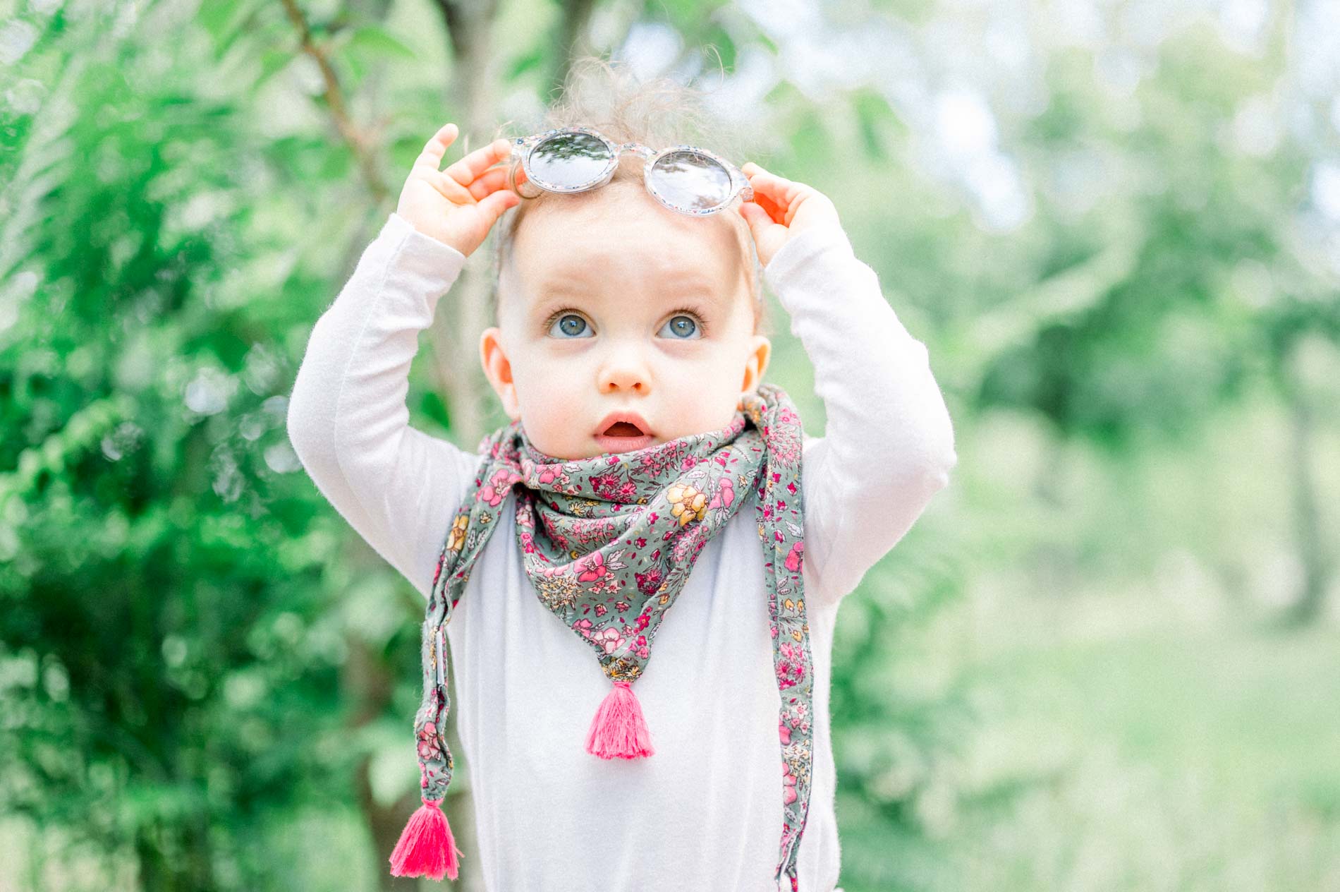 Baby pushing sunglasses up onto their head in the greenery