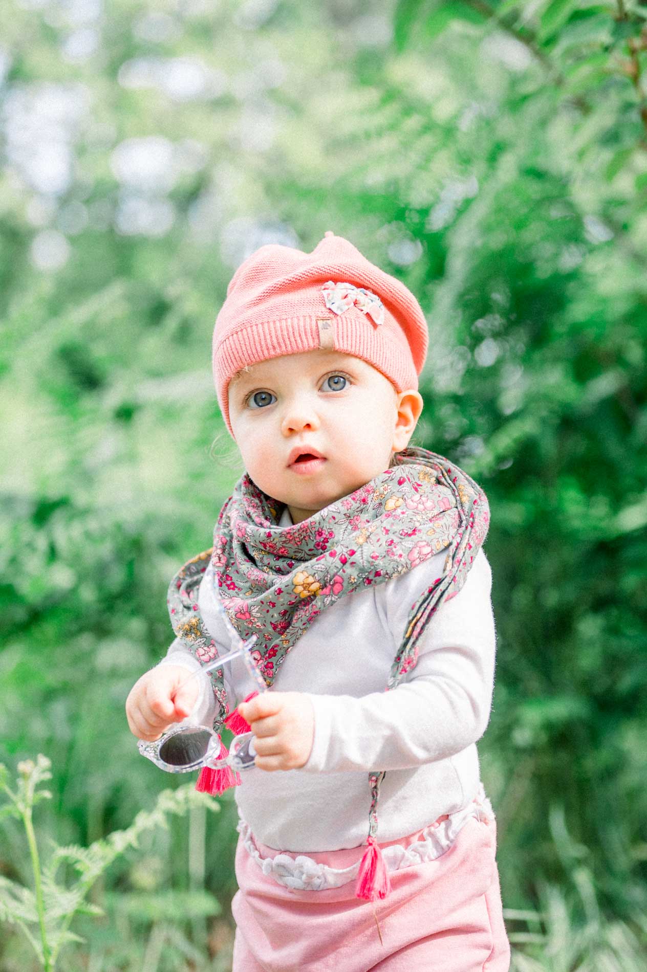 Baby in a pink beanie and floral scarf among the ferns