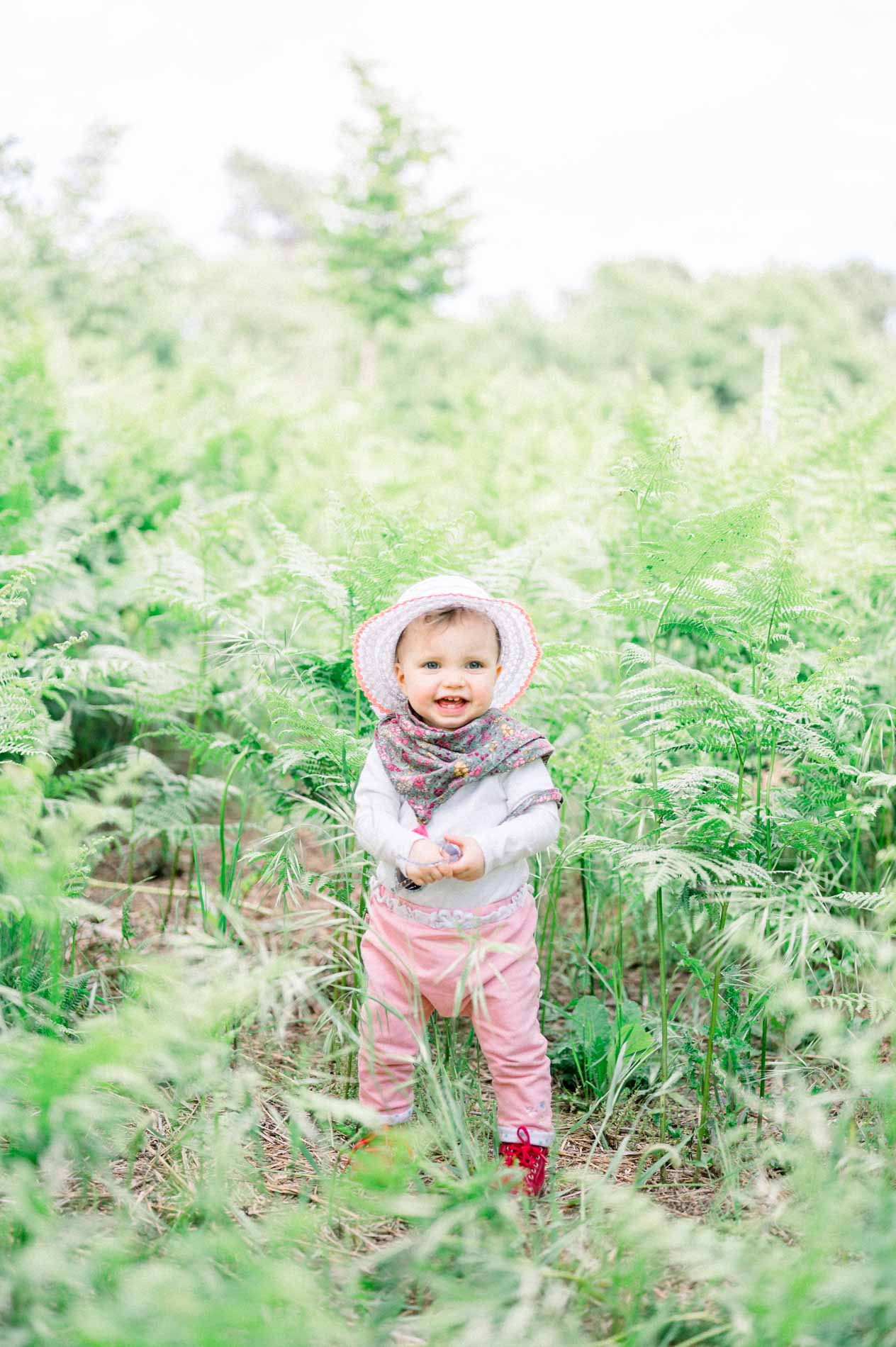 Baby in a sunhat walking through tall ferns