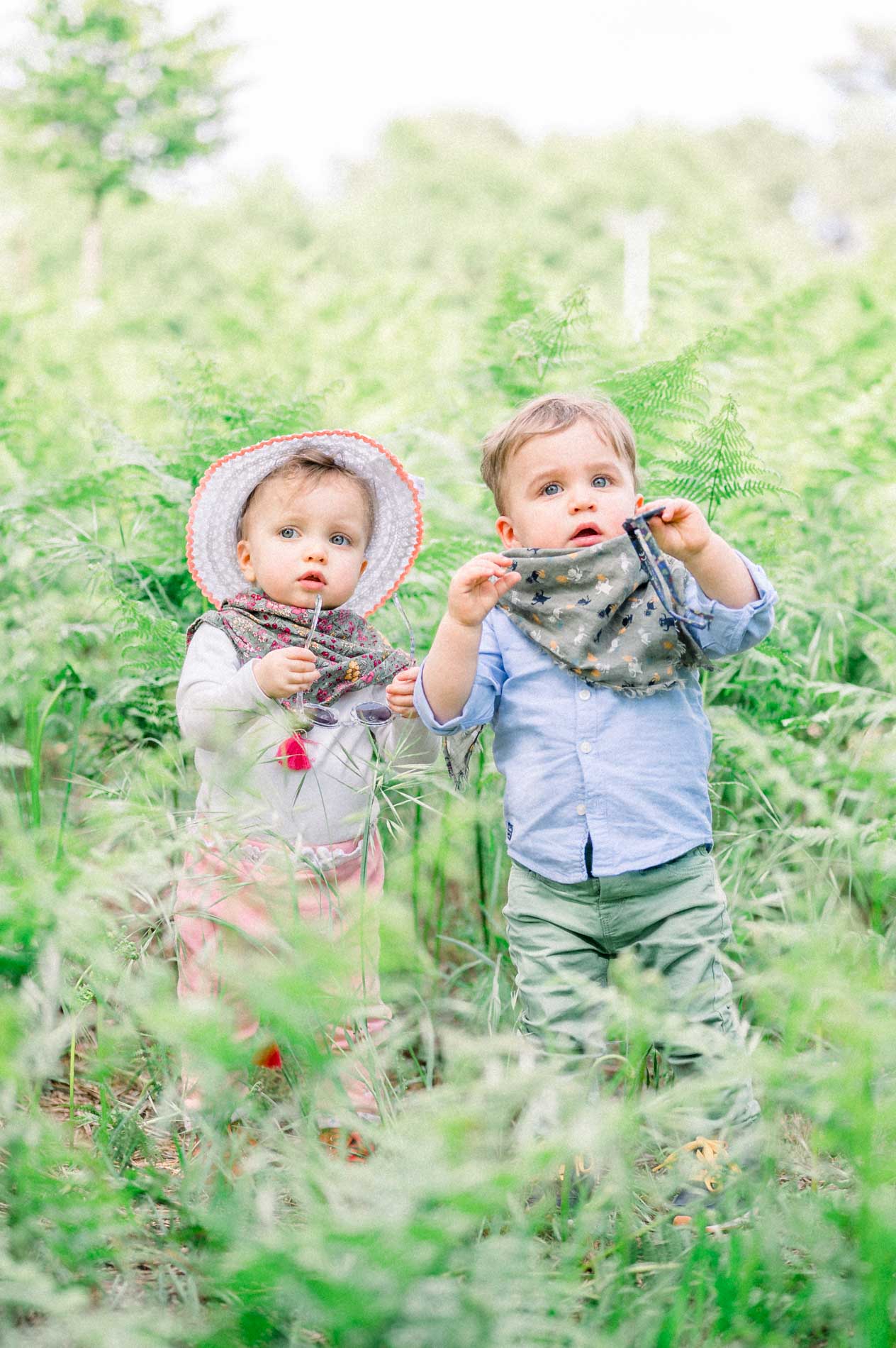 Two young siblings side by side in the ferns wearing floral scarves
