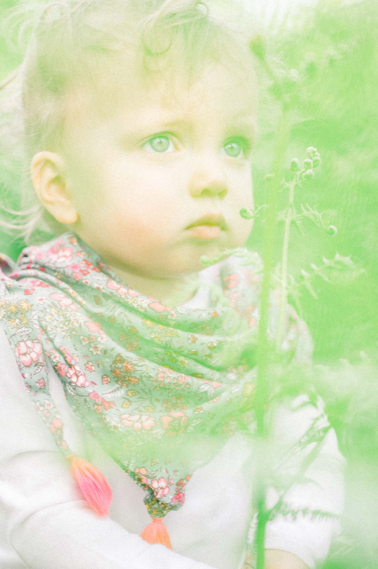 Portrait of a baby in a floral scarf through a veil of green foliage