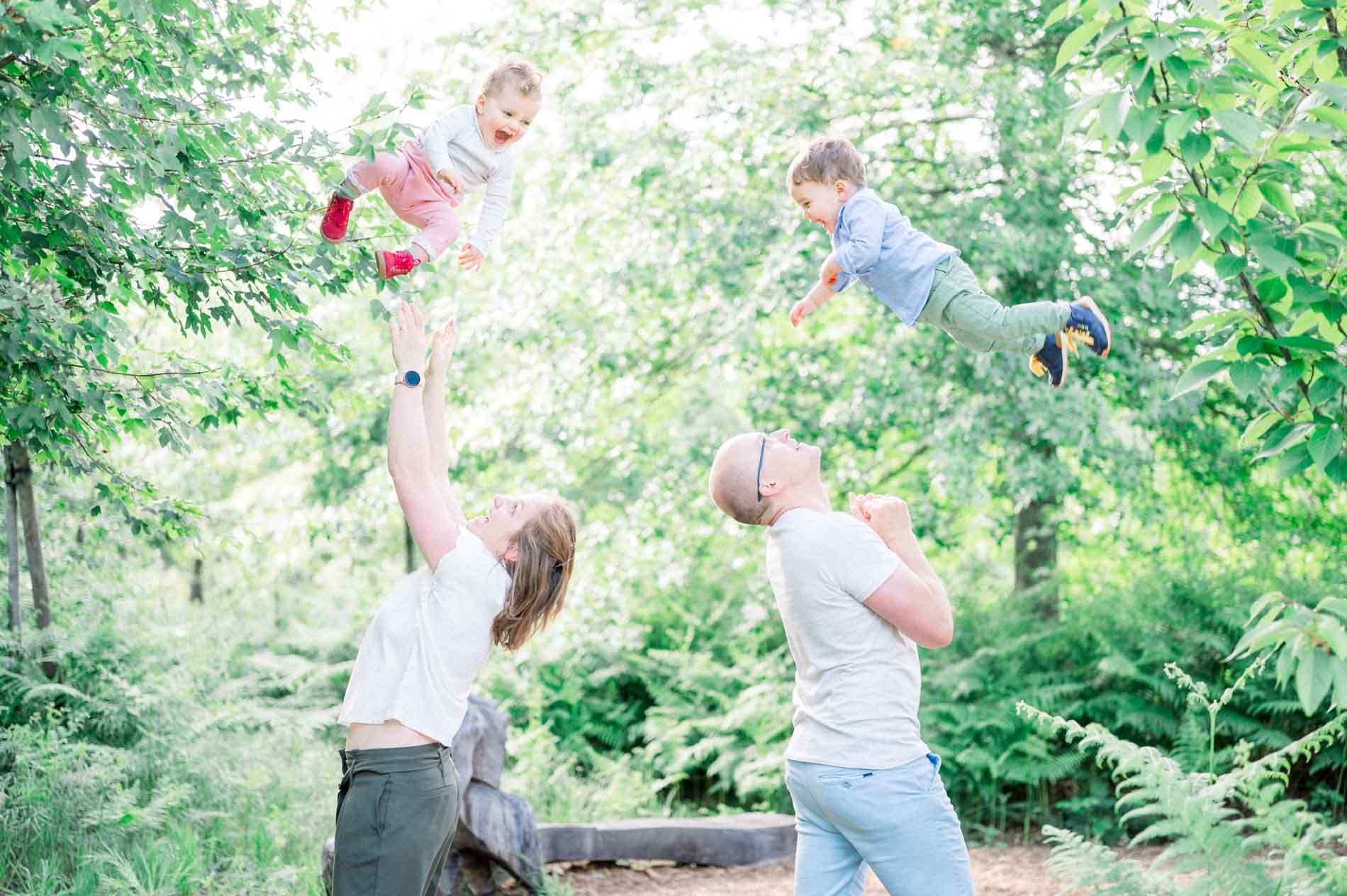 Parents lifting their two little ones high in the air in the woods during a lifestyle family session