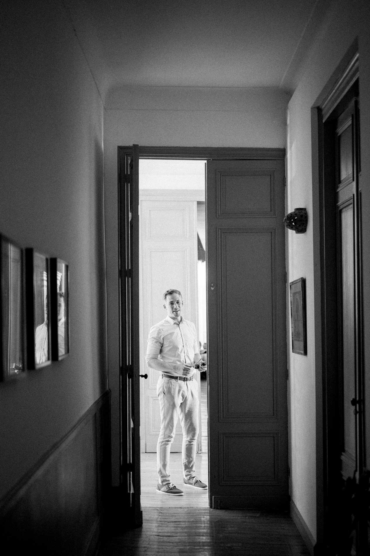 Groom appearing at the end of a hallway through an open door, black and white
