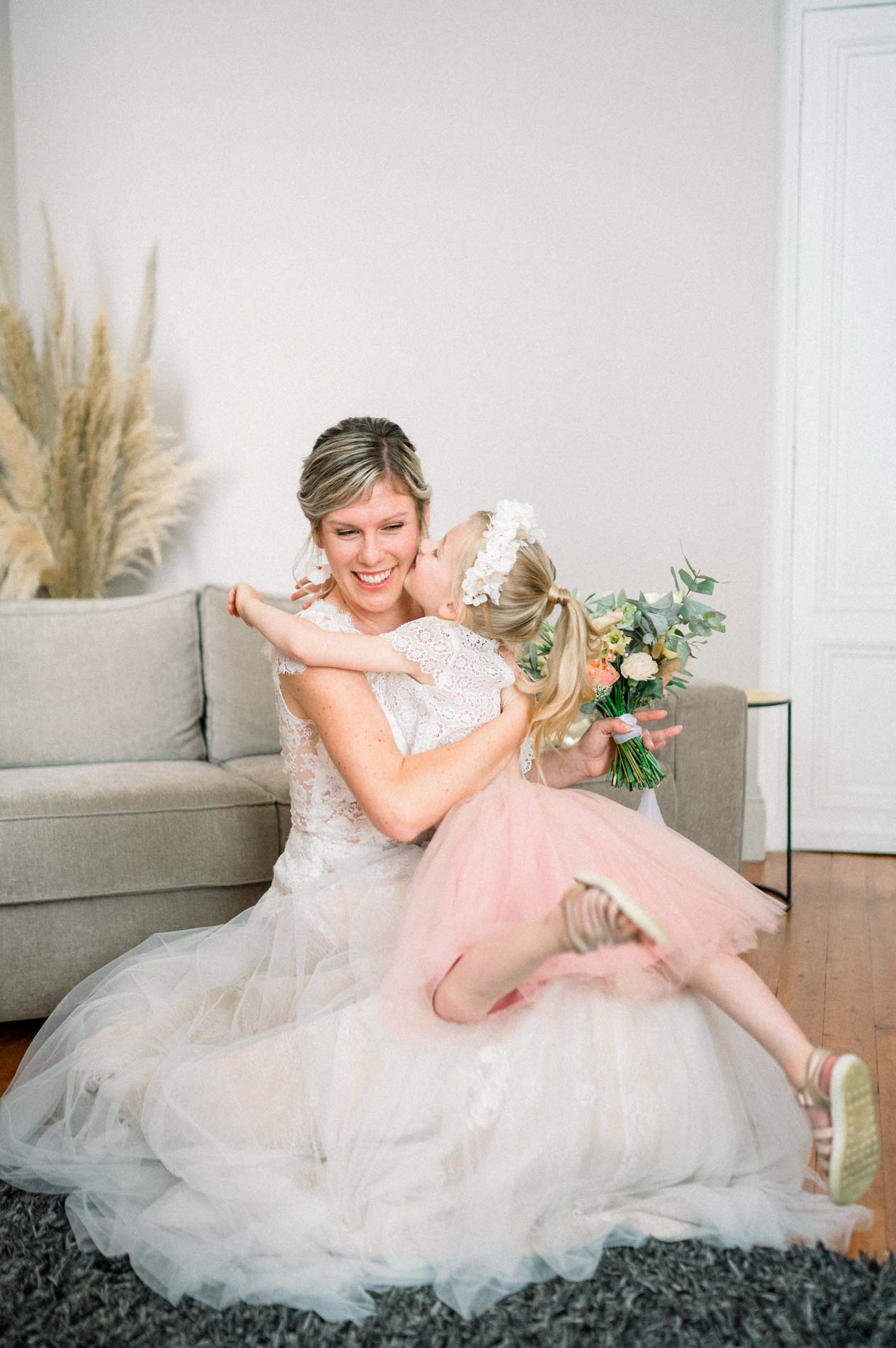 Bride hugging a little girl in a pink dress on the sofa