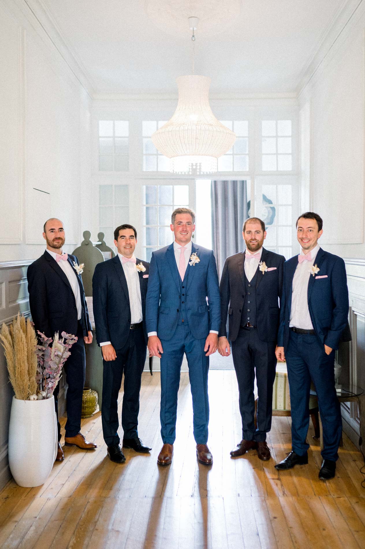 Groom and his groomsmen in blue suits beneath the Chartreuse chandelier