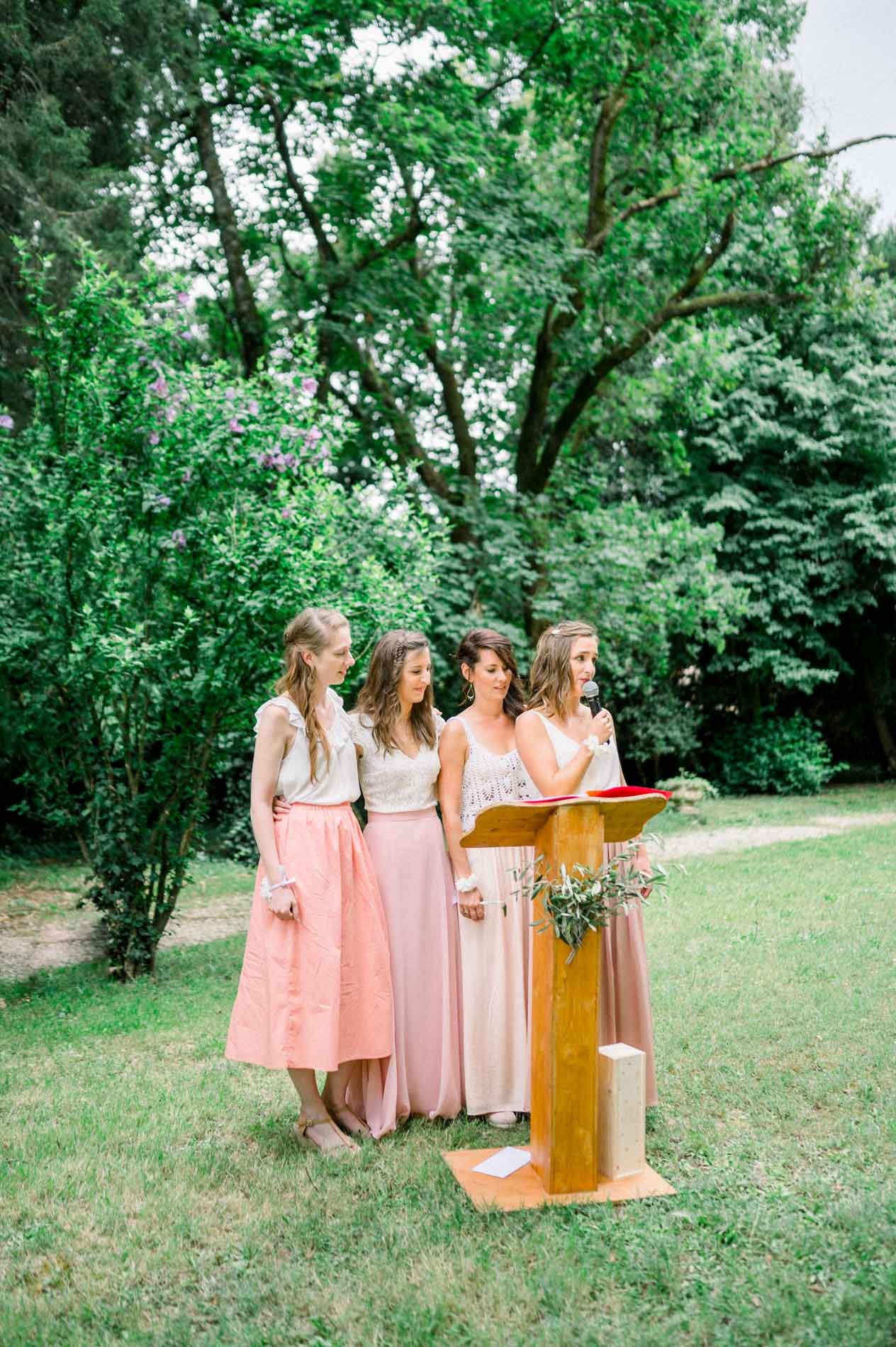 Three bridesmaids in pink skirts reading a speech at the lectern